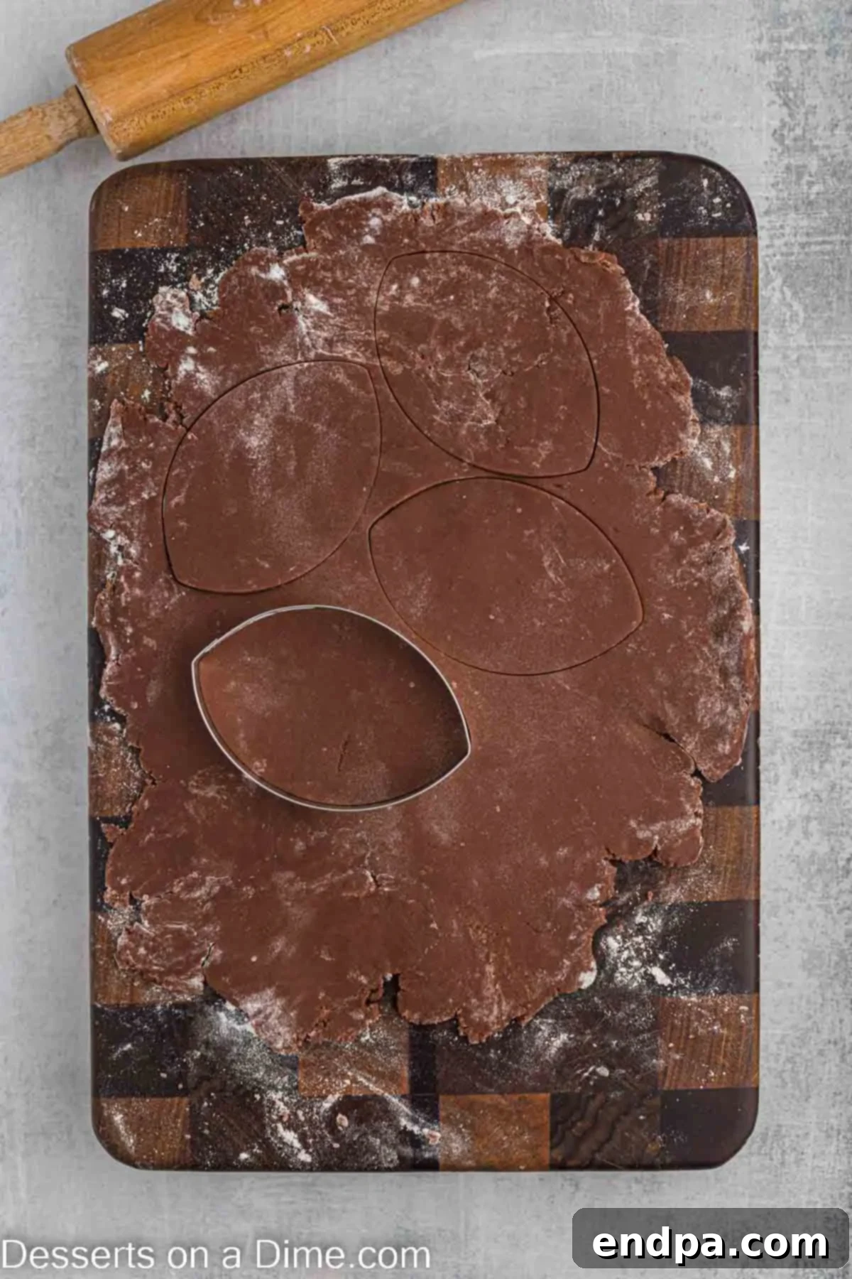Championship Chocolate Football Cookies 7 Cookie dough rolled out on a floured surface, with football shapes being cut out using a cookie cutter.