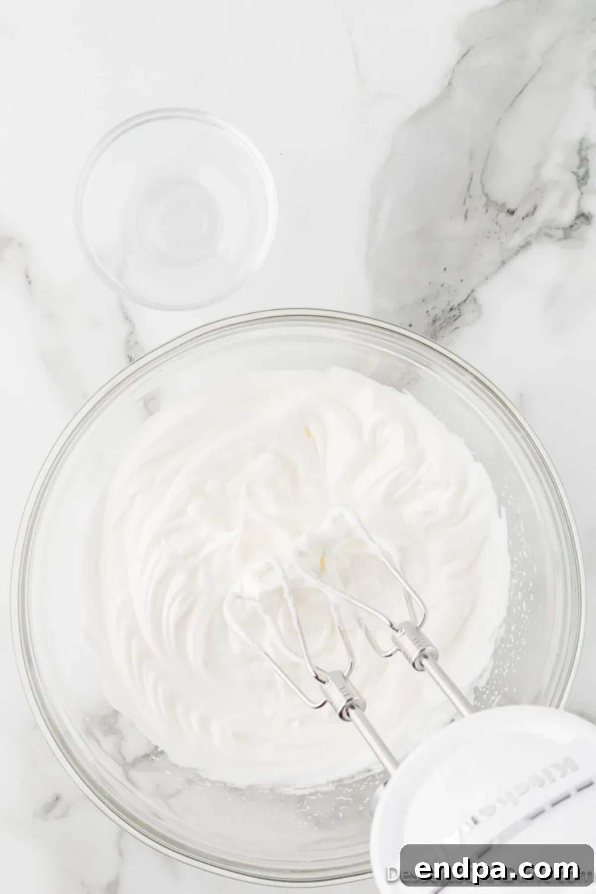 Velvety Chocolate Bliss 10 Egg whites being whipped in an electric mixer, forming foamy peaks that are beginning to stiffen.