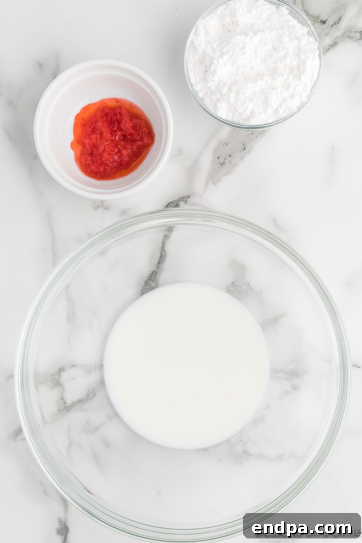 Ingredients for the strawberry glaze, including powdered sugar, strawberry puree, and milk, being whisked in a bowl.