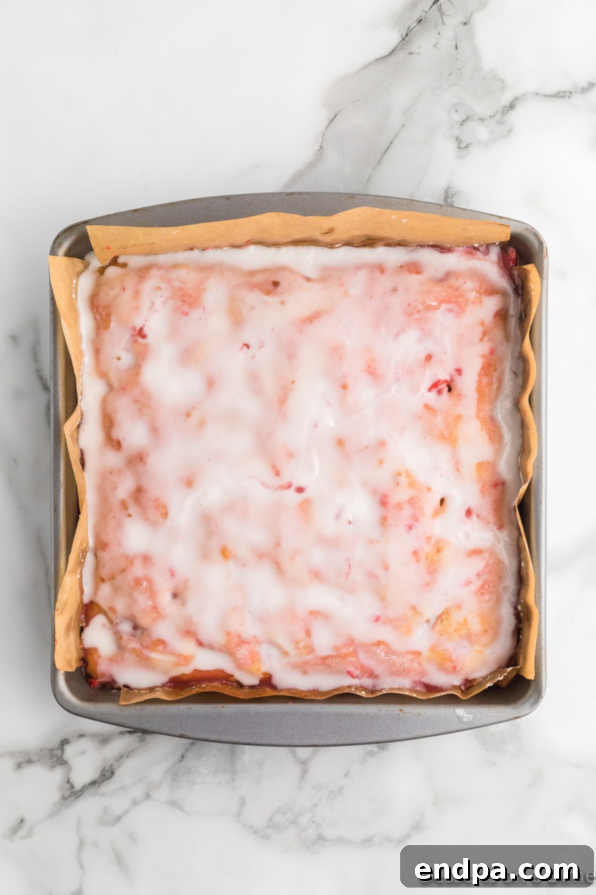 Strawberry glaze being spread evenly over the cooled Strawberry Lemon Blondies with a spatula.