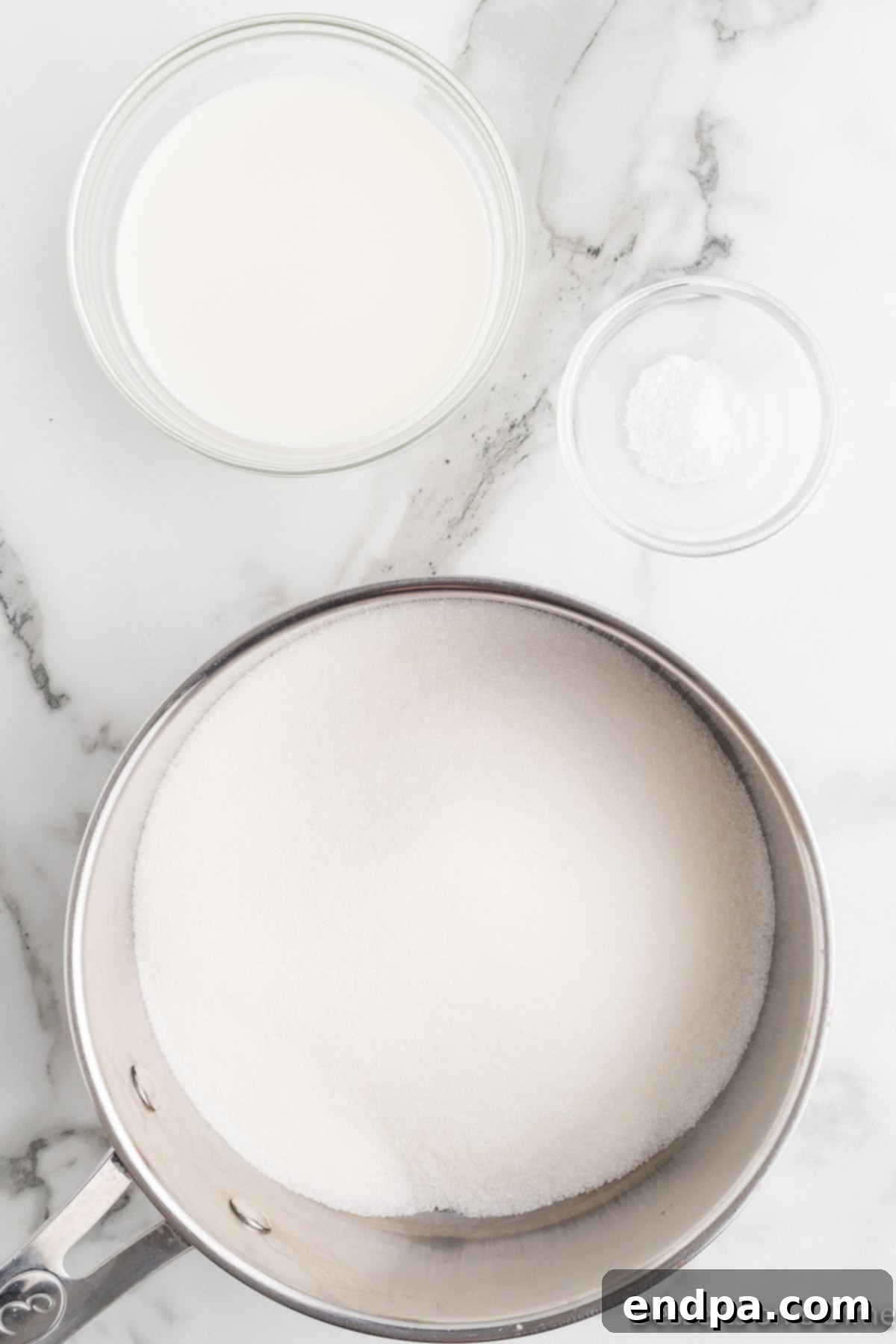 A saucepan on the stove with the sugar, milk, corn syrup, and salt mixture, being whisked to dissolve the sugar.