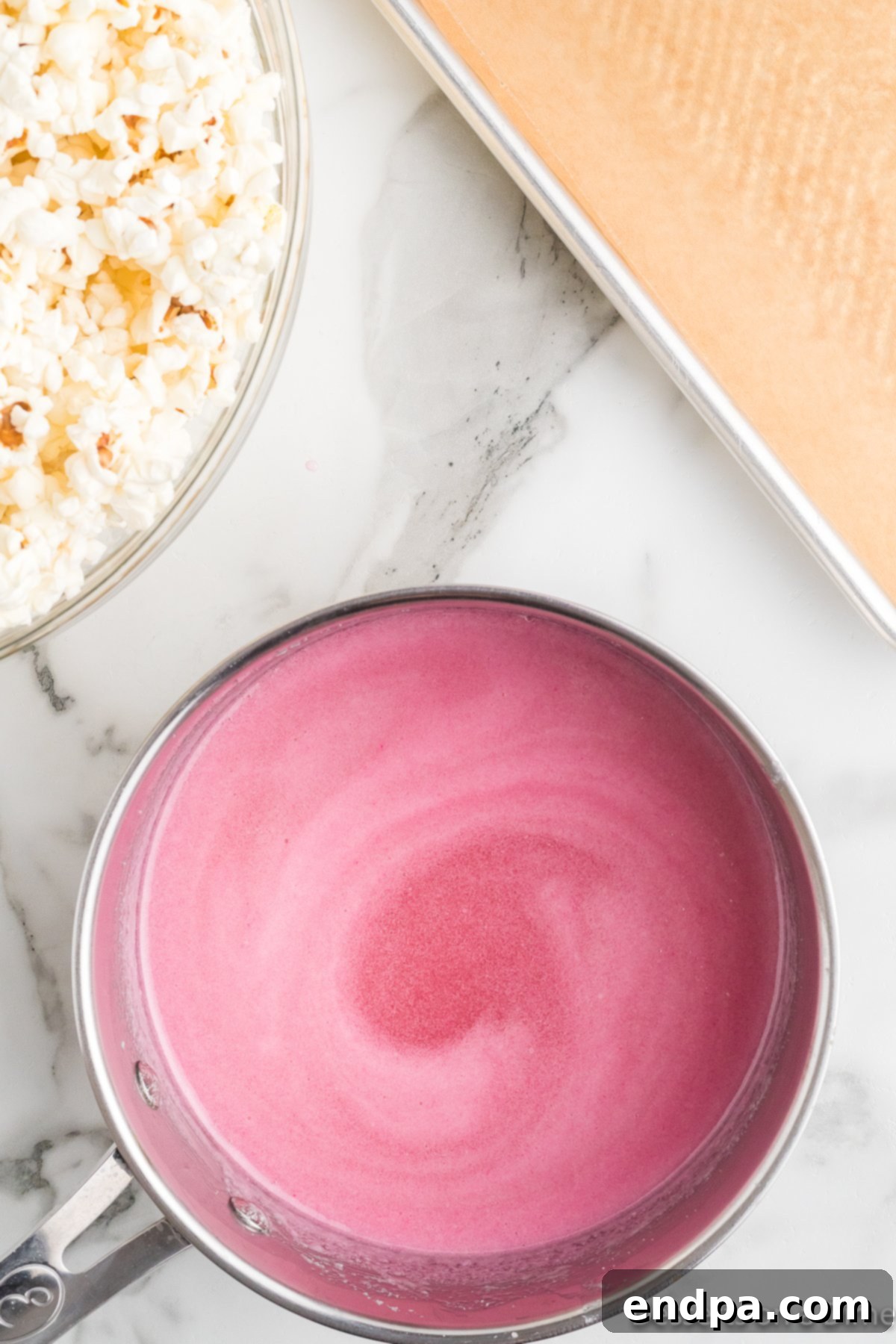 Pink food coloring mixed into the hot sugar mixture in a pan, turning it a vibrant pink hue.
