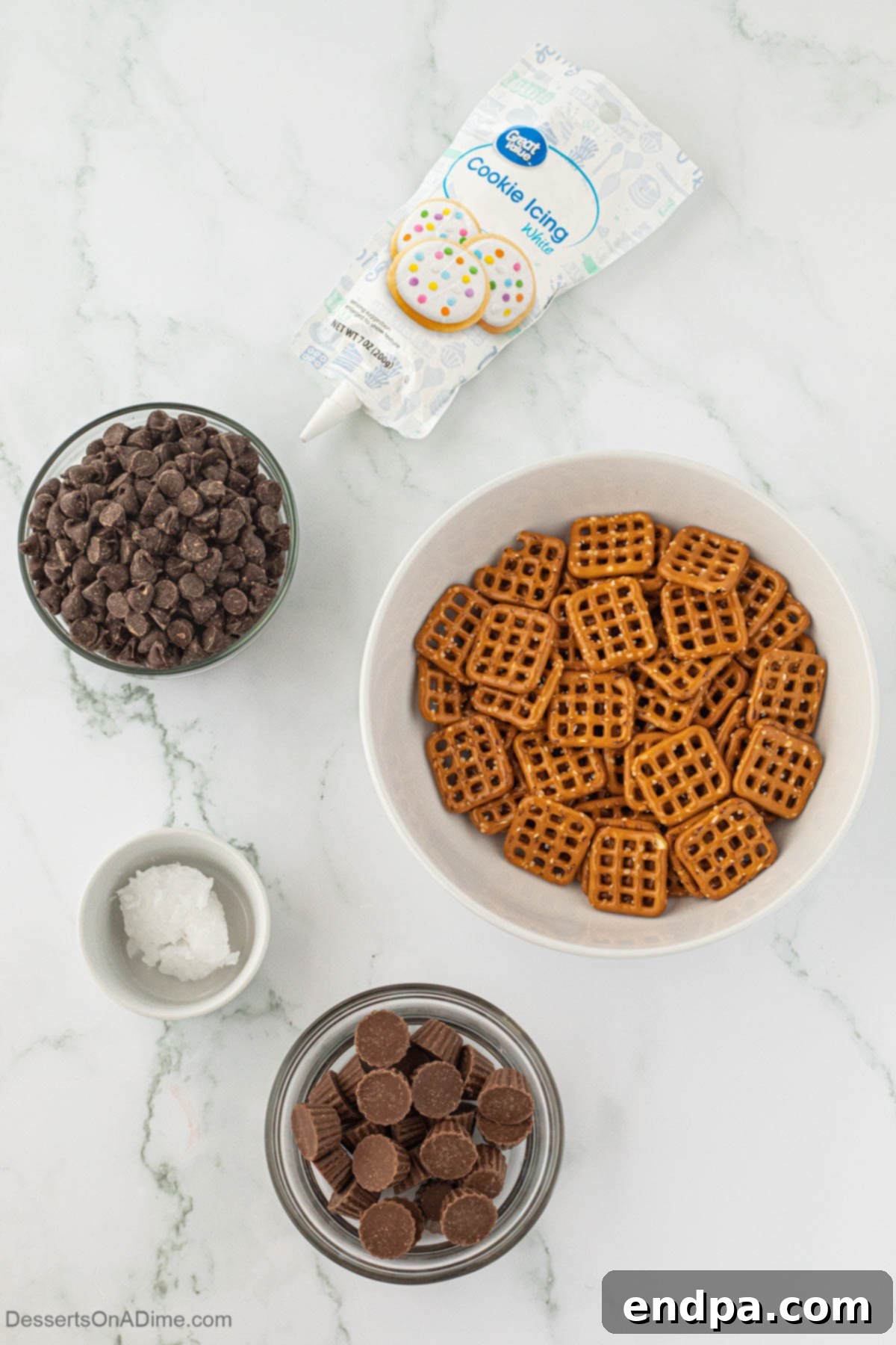 Ingredients for Chocolate Covered Pretzel Cookies - pretzels, Reese's peanut butter cups, chocolate chips, white icing laid out on a table.