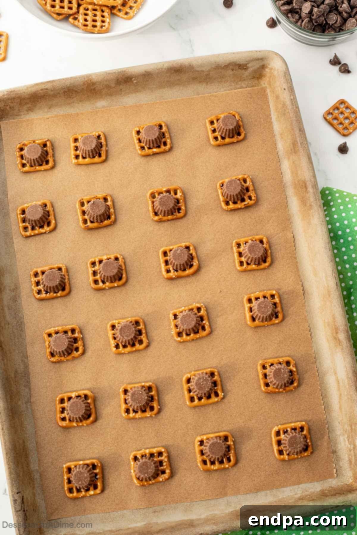 Pretzels topped with an unwrapped peanut butter cup on a baking sheet.