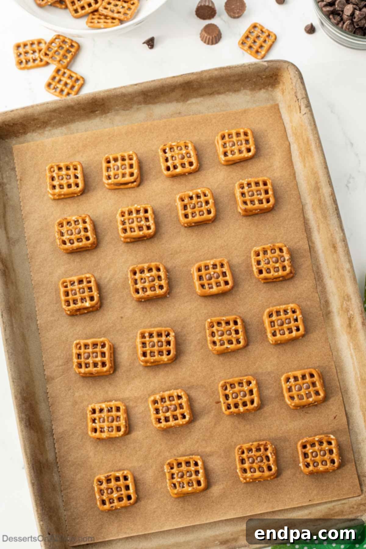 Another pretzel being placed on top of a melted peanut butter cup and pretzel base.