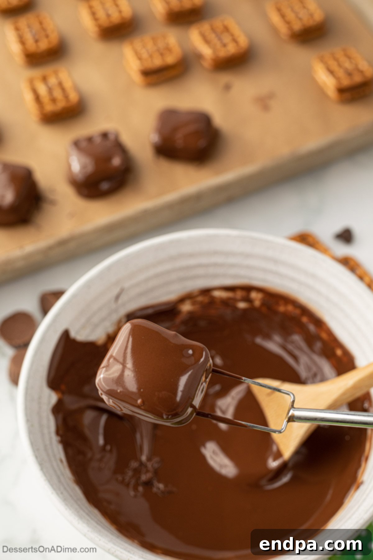 A pretzel sandwich being dipped into melted chocolate with a fork.
