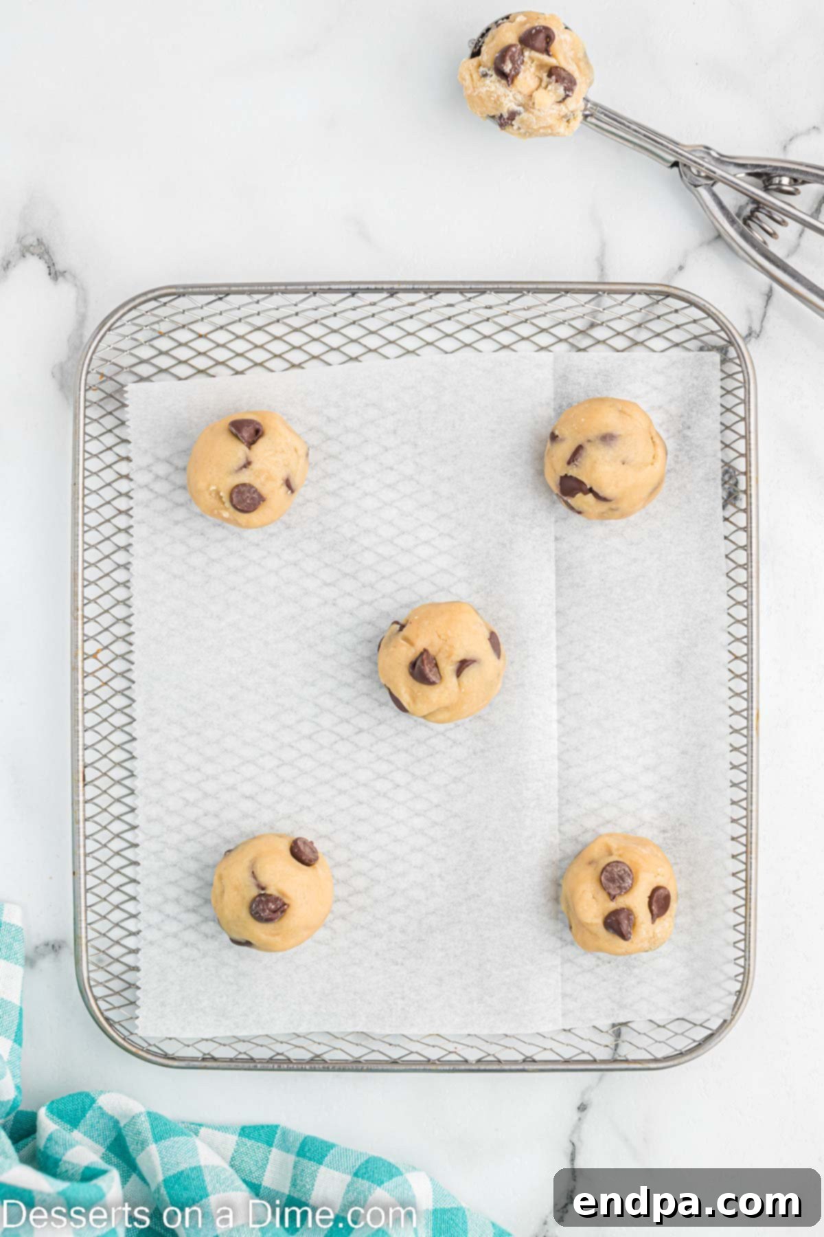 Raw cookie dough balls arranged on a piece of parchment paper inside an air fryer basket, ready for cooking.