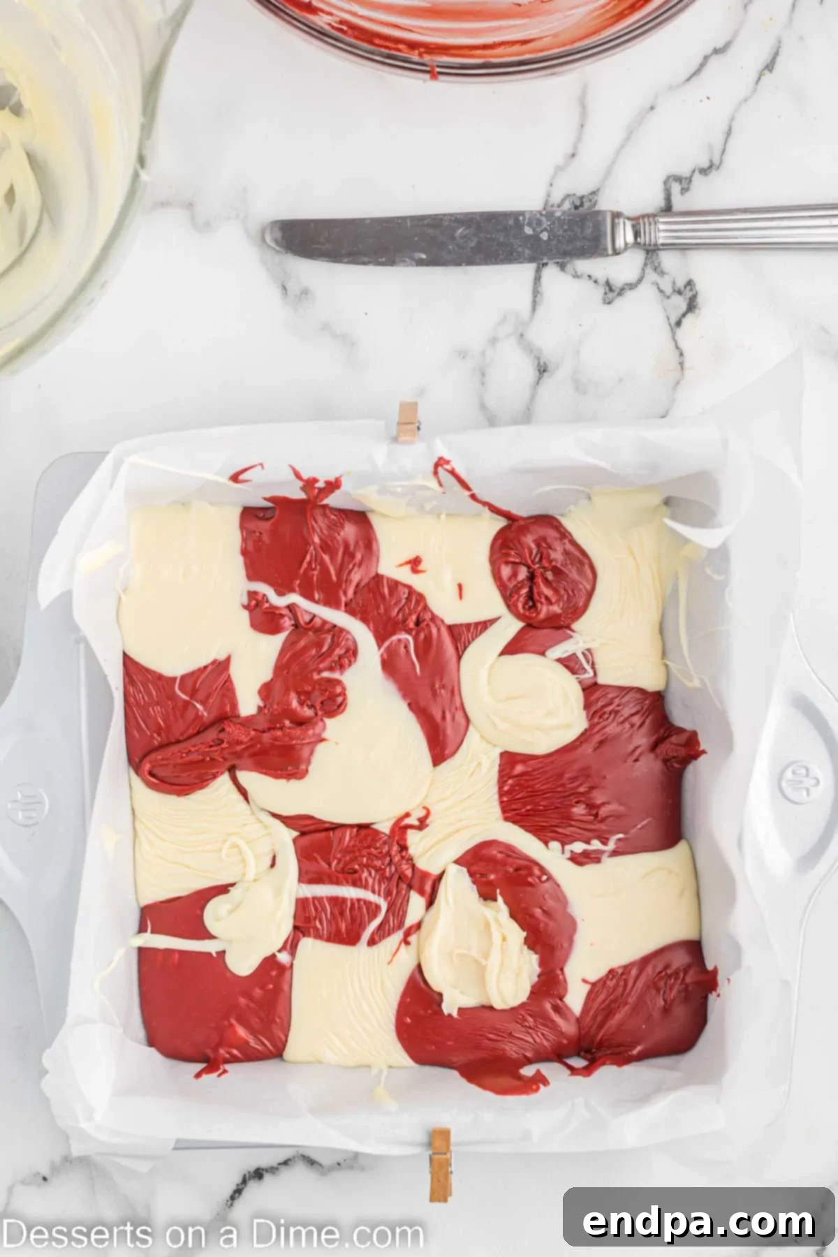 Alternating spoonfuls of red and white fudge mixture spread into a parchment-lined baking dish.