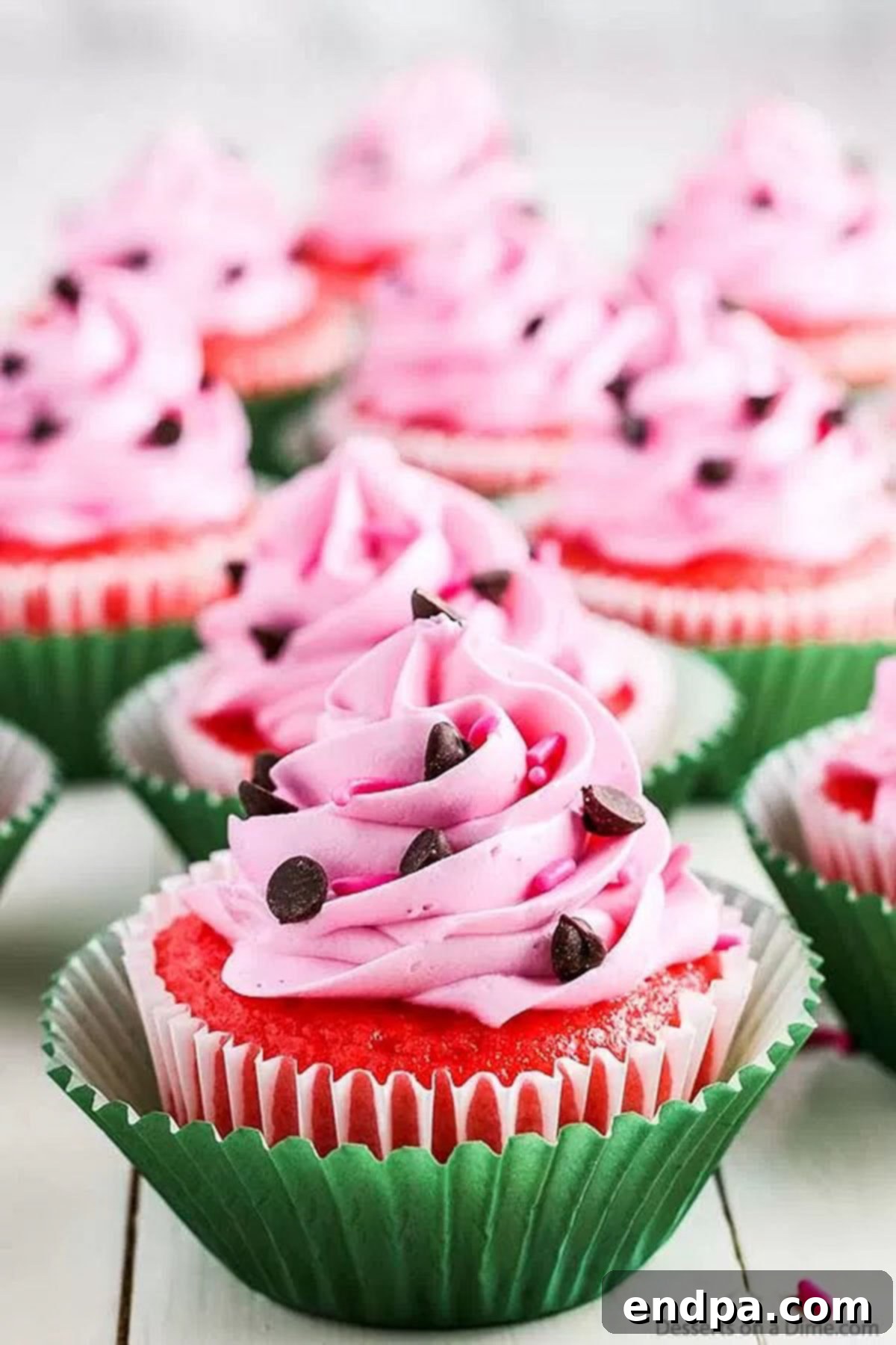 Serve up a slice of summer with these fun and flavorful watermelon cupcakes! Watermelon cupcakes ready to serve, showcasing their vibrant pink color and chocolate chip 'seeds'.