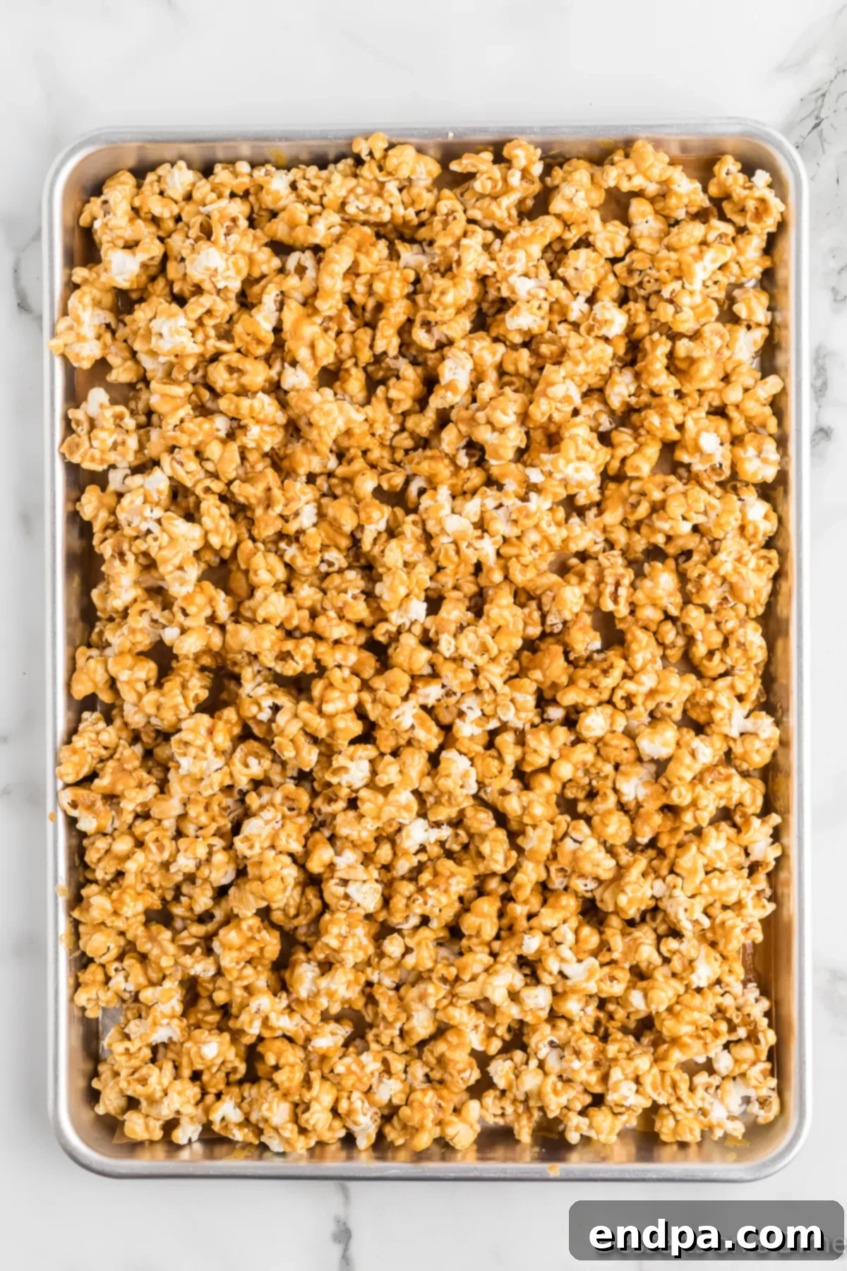 Freshly popped popcorn coated with caramel mixture on a baking sheet. 