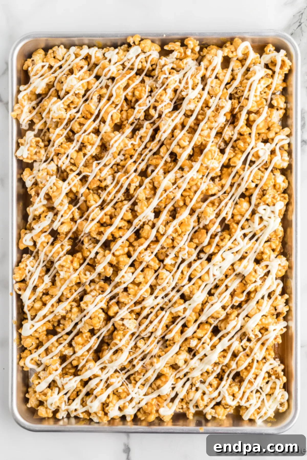Caramel popcorn drizzled with melted white chocolate on a baking sheet. 