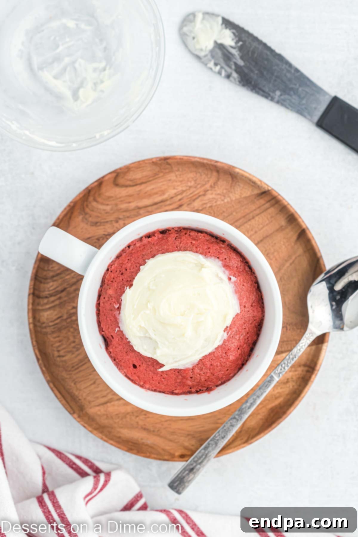 Cream cheese frosting being spread smoothly on top of the cooled Red Velvet Mug Cake