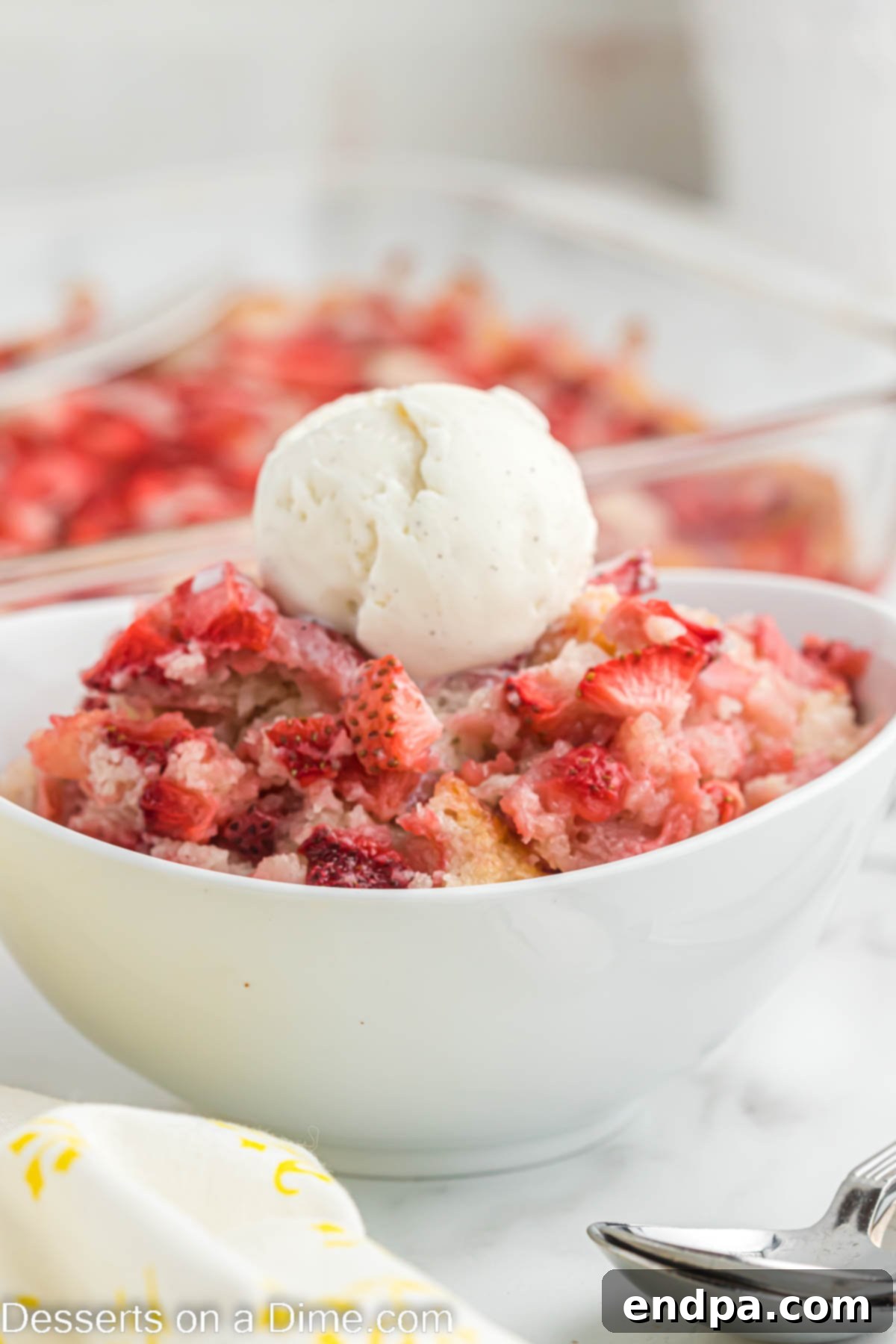 A warm bowl of strawberry cobbler topped with a scoop of melting vanilla ice cream.