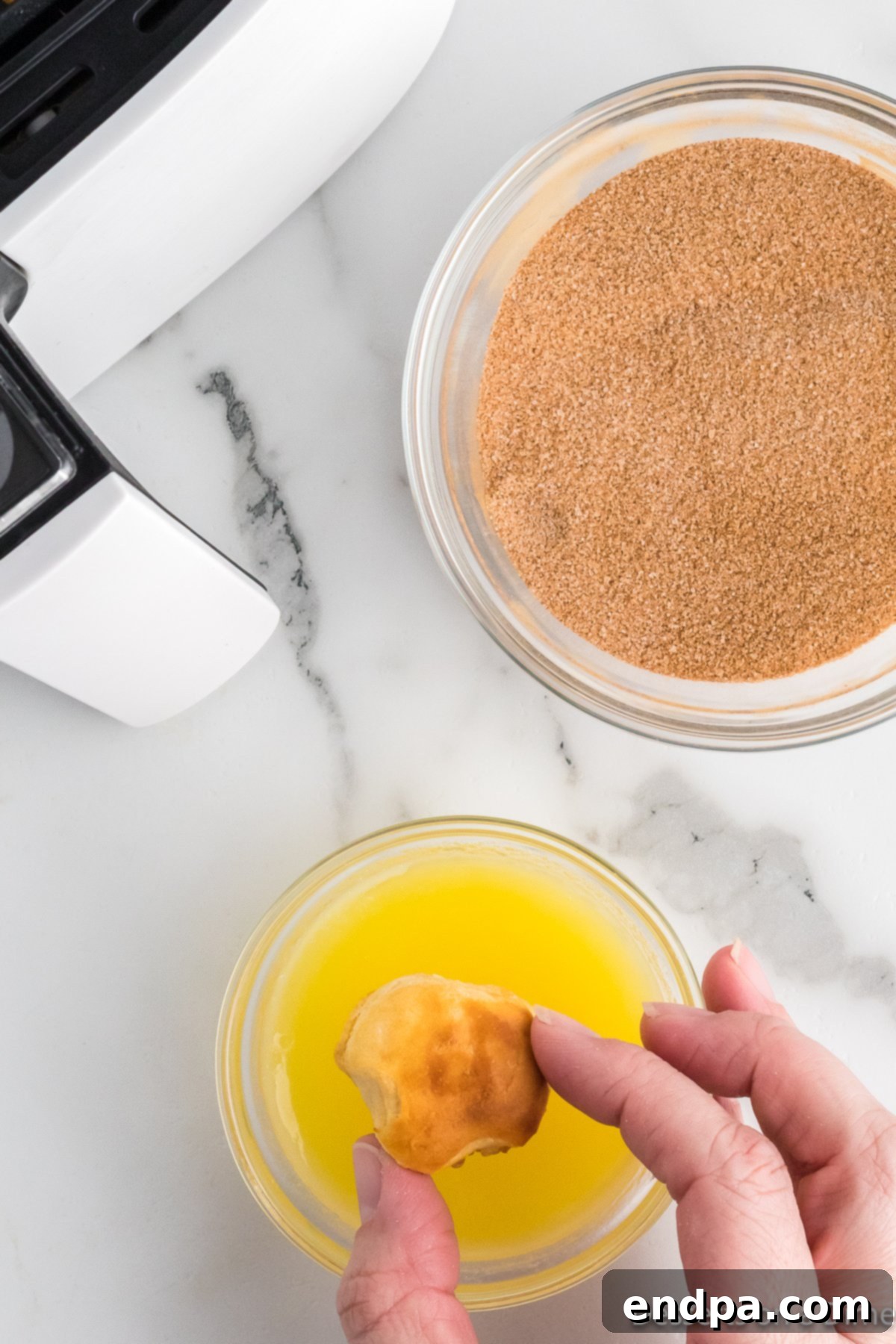 Air Fryer Donut Poppers 8 A donut hole being dipped first into melted butter and then into a bowl of cinnamon sugar.