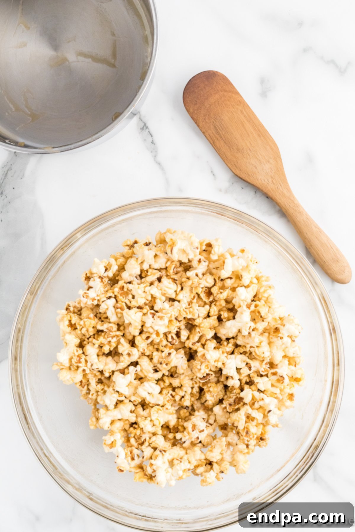 Popcorn in a bowl being tossed with the honey butter glaze to coat evenly.