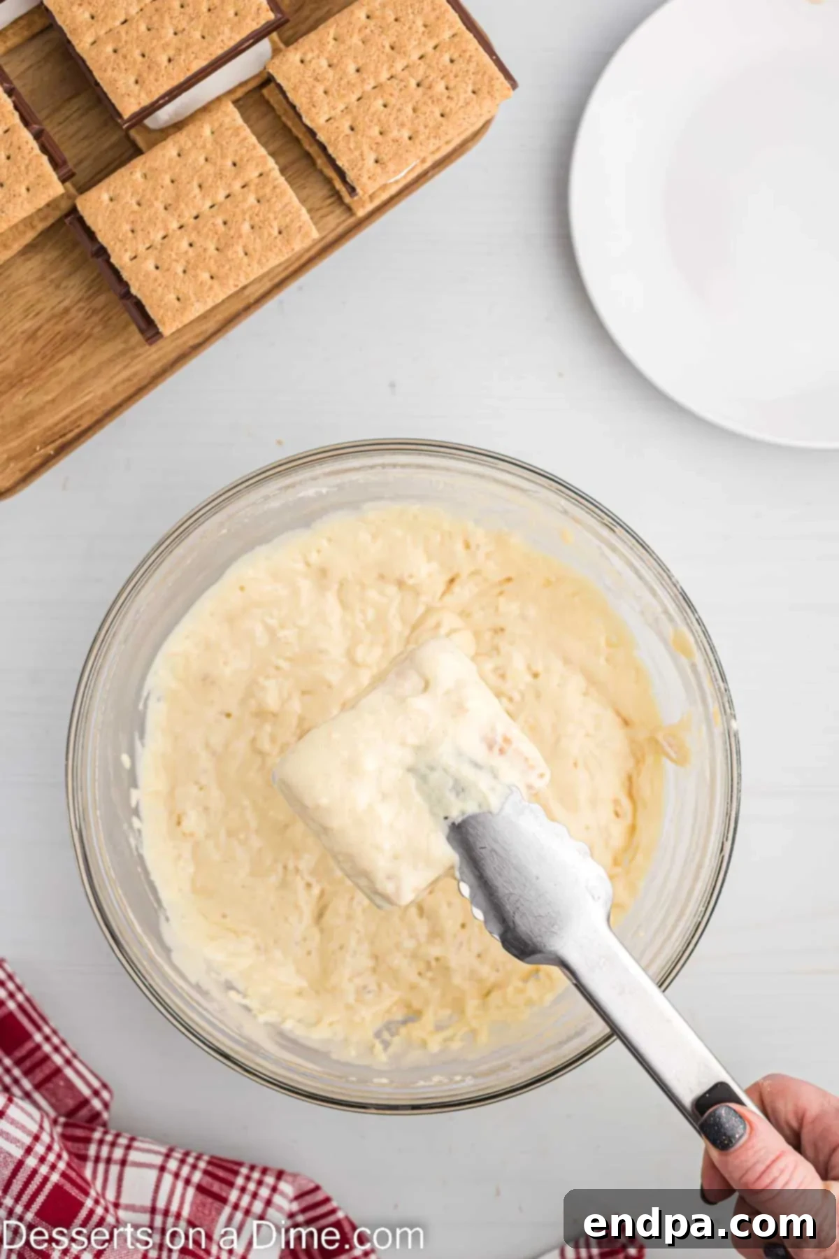 Crispy Golden Smores Delight 6 Assembled S'mores being dipped into the prepared pancake batter with tongs.
