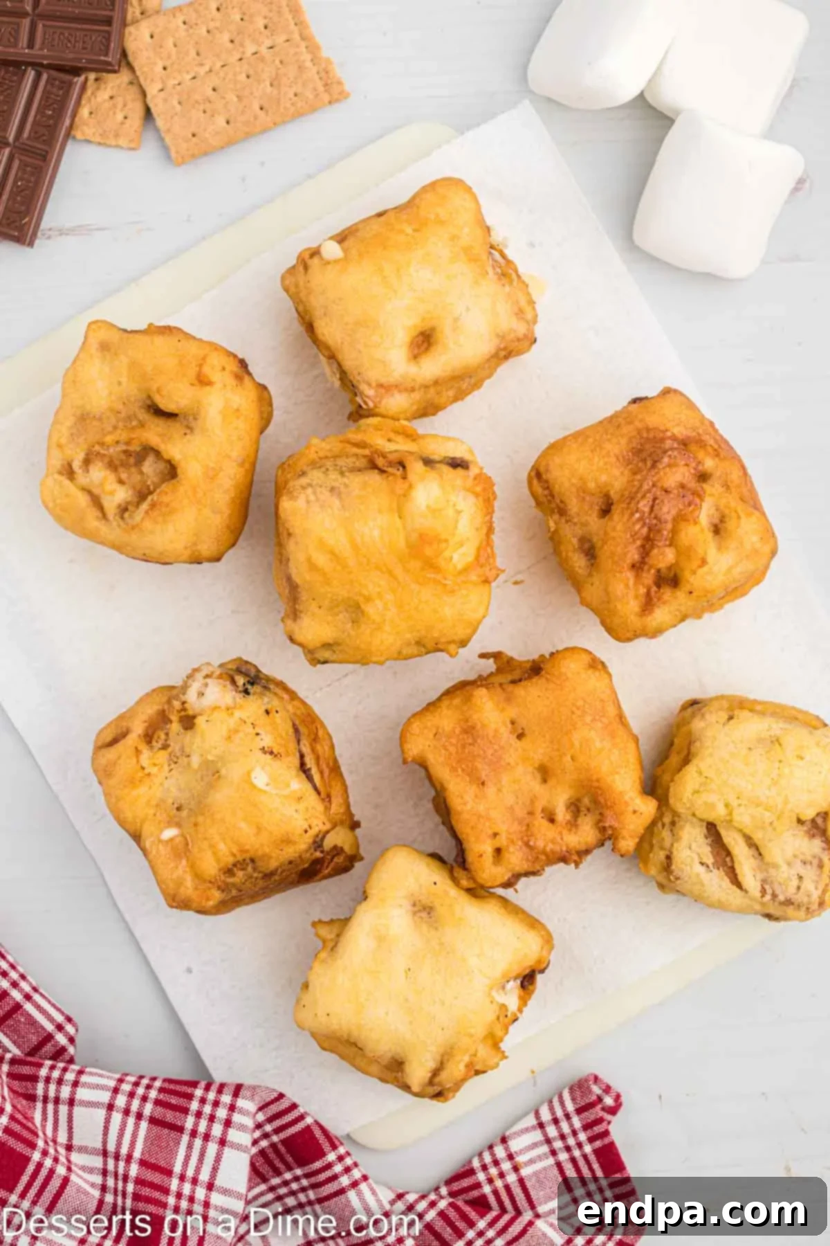 Crispy Golden Smores Delight 7 Freshly fried S'mores cooling on a wire rack, with a paper towel beneath to absorb excess oil.