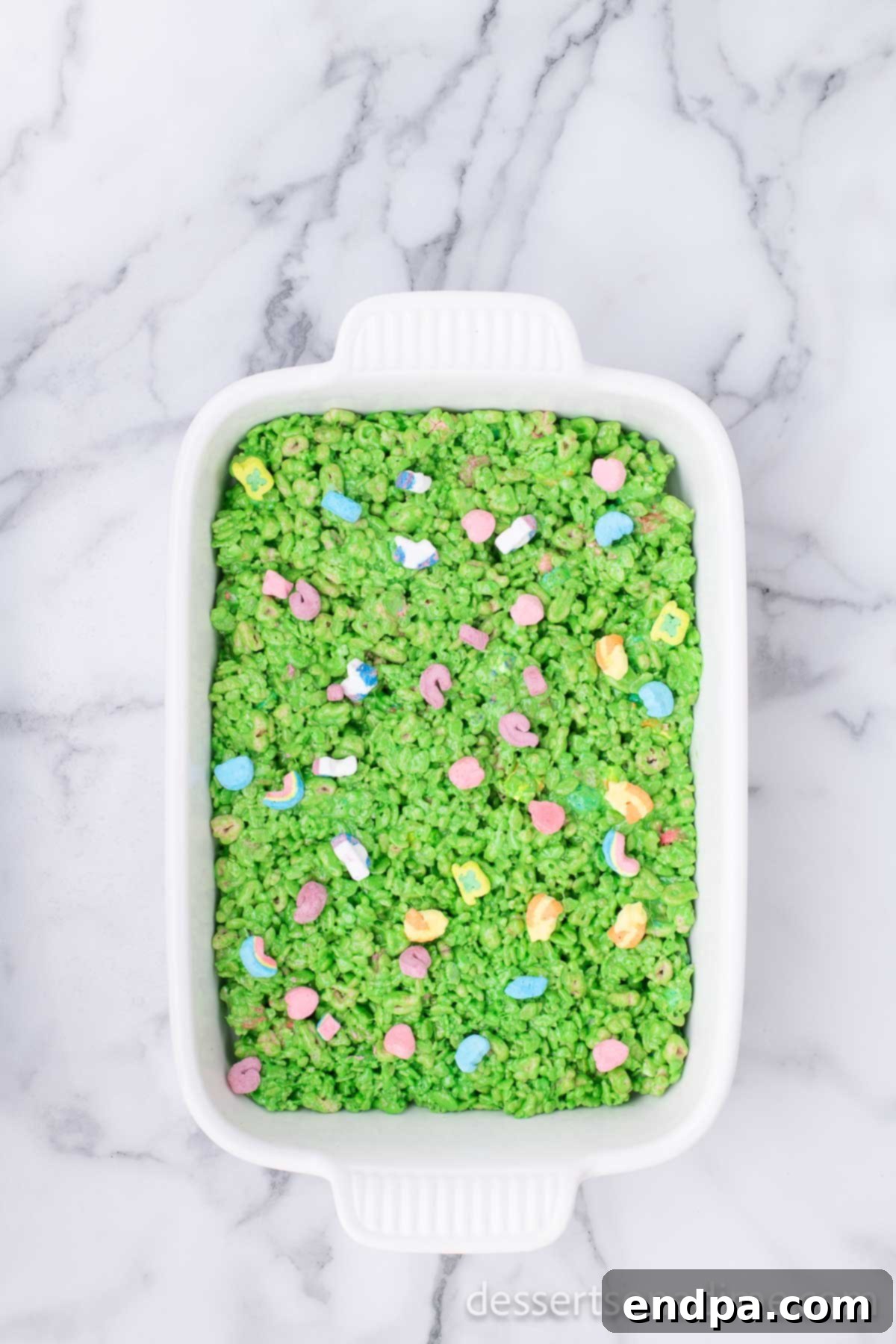 Shamrock Krispie Squares 8 More Lucky Charms marshmallows sprinkled generously on top of the green cereal treats in the baking dish.