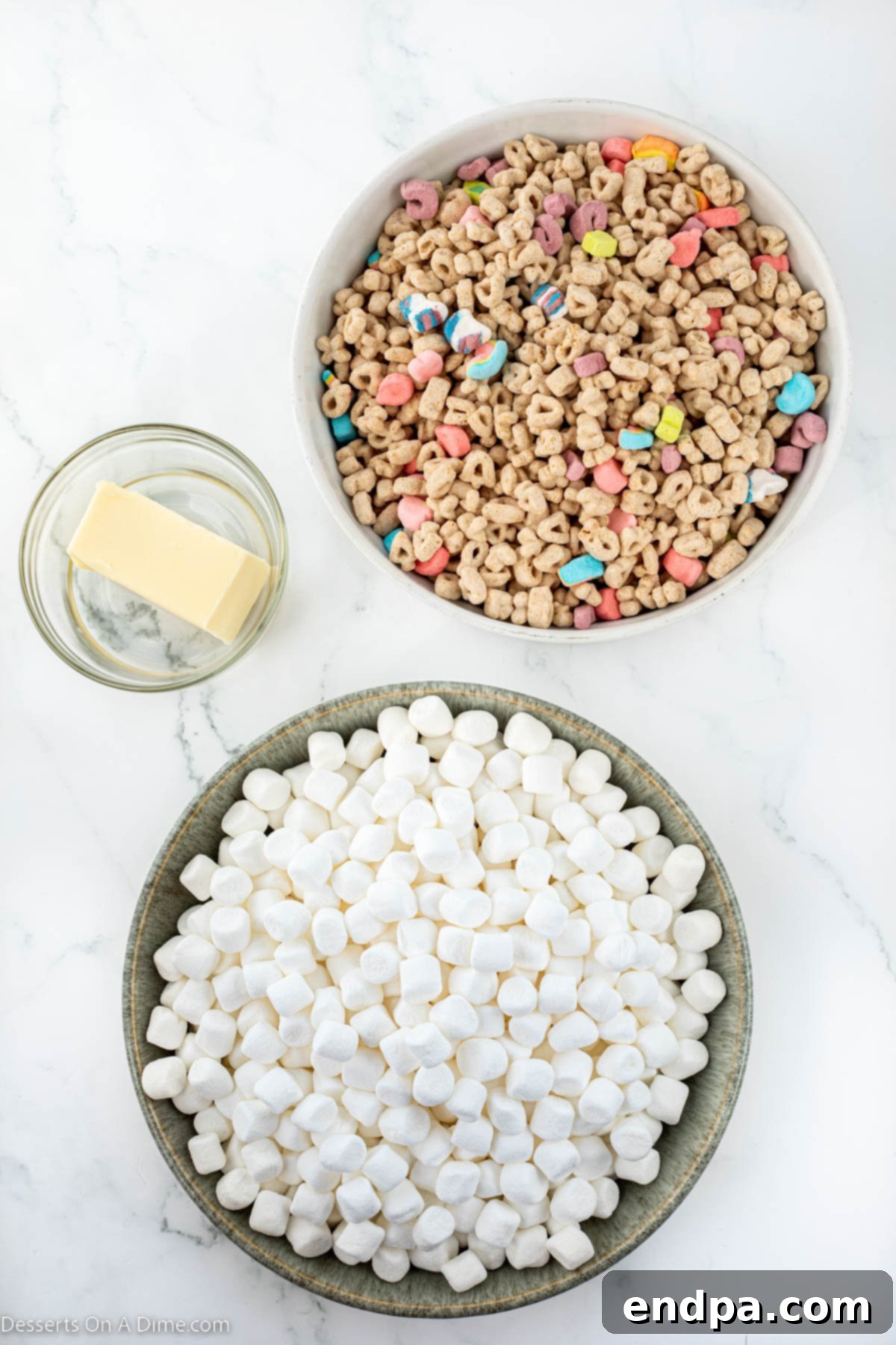 Three core ingredients for Lucky Charm Treats: a bag of mini marshmallows, a stick of butter, and a box of Lucky Charms cereal.