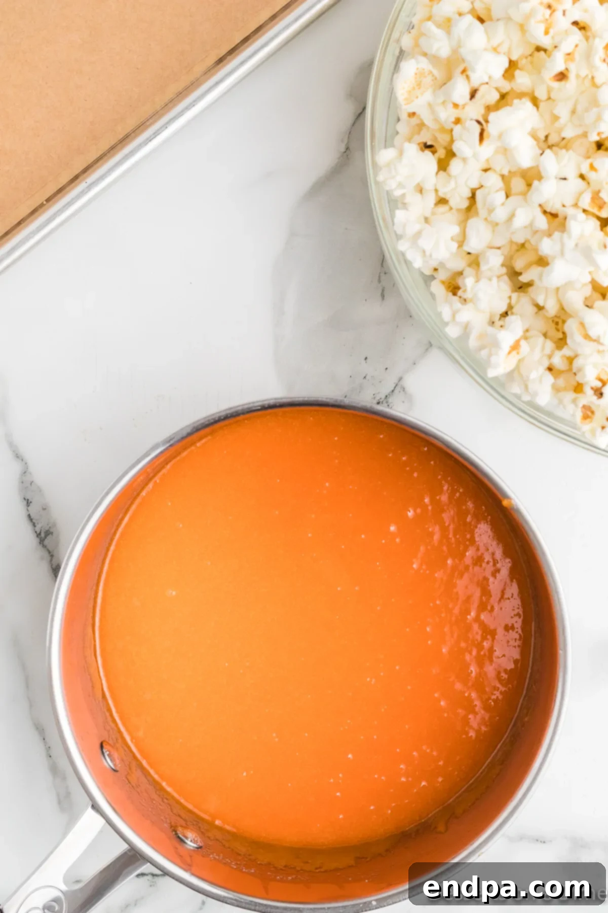 Rainbow Jello Popcorn Delight 5 Jello mixed into the melted butter. A vibrant, red Jello powder has just been stirred into the melted butter, sugar, and corn syrup mixture in a saucepan. The mixture is swirling, showing streaks of red against the golden syrup, indicating the beginning of its transformation into a colorful candy coating.