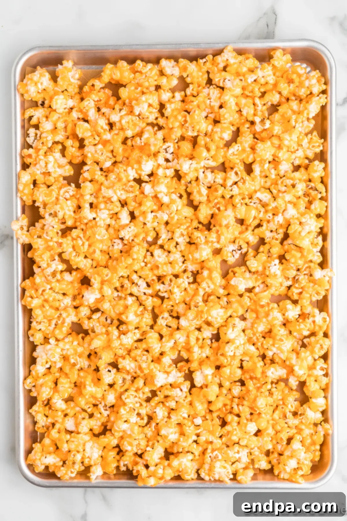 Rainbow Jello Popcorn Delight 6 Jello Popcorn spread on baking sheet. A generous amount of freshly coated Jello popcorn, vibrant red in color, is evenly spread across a large baking sheet lined with parchment paper. The popcorn kernels are distinct and glistening, ready for baking to achieve their crispy texture.