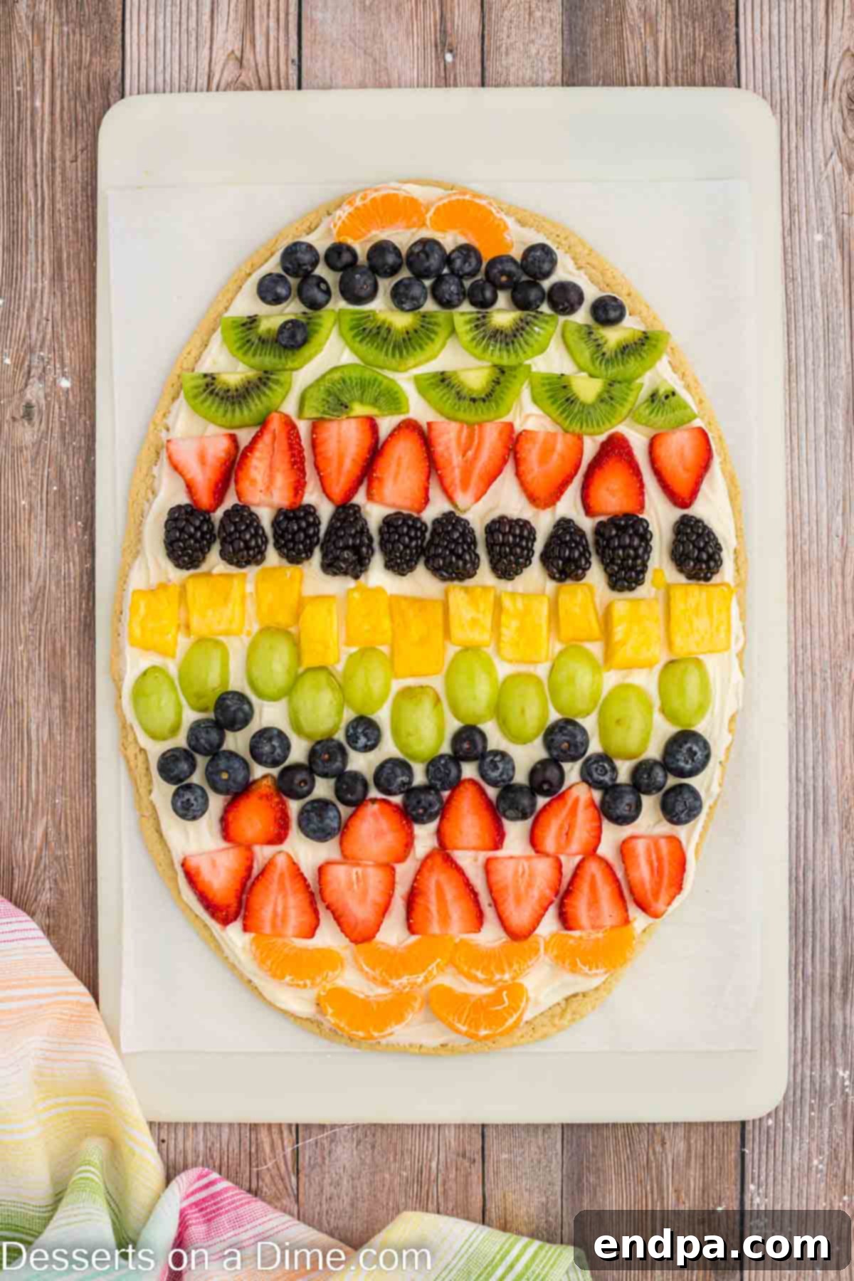 An Easter Egg Fruit Pizza with a smooth layer of cream cheese frosting applied, ready for fruit decoration.