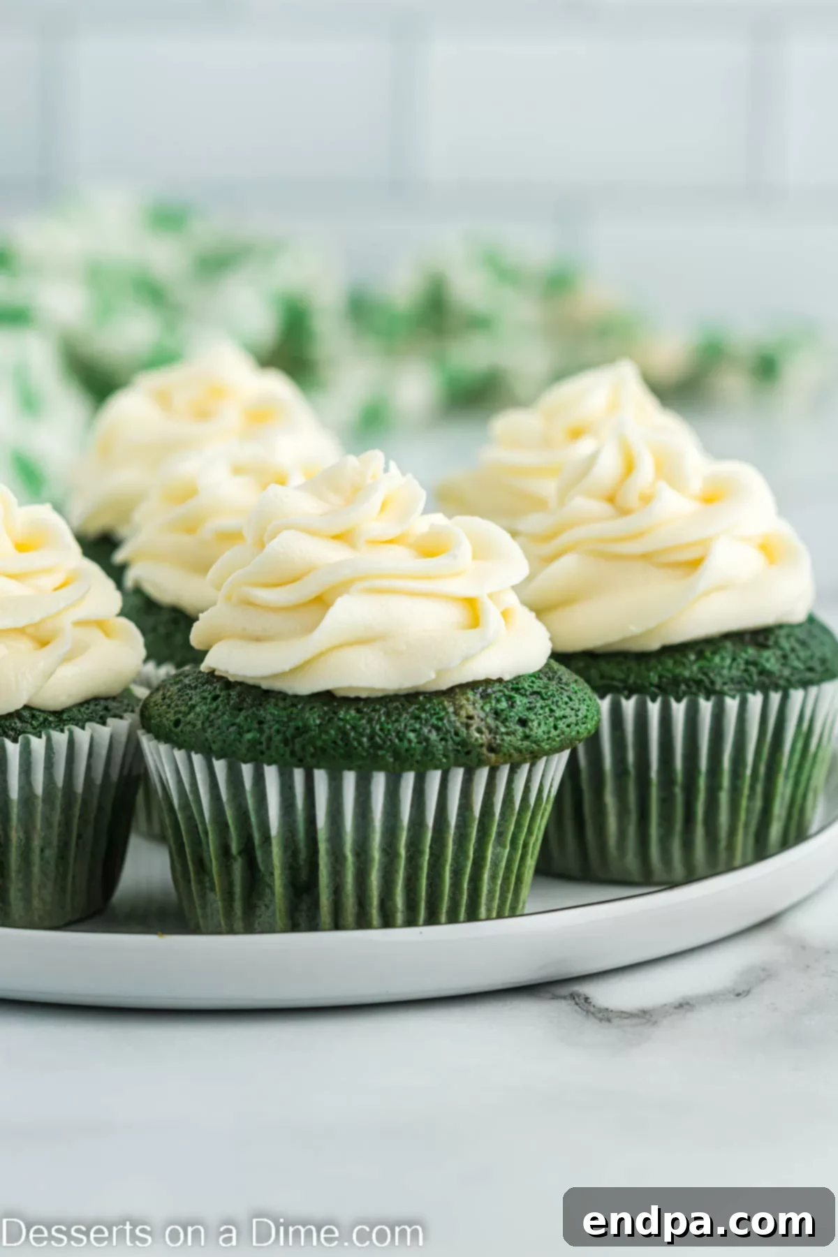 A vibrant display of green velvet cupcakes, beautifully frosted with white cream cheese, arranged on a rustic platter.