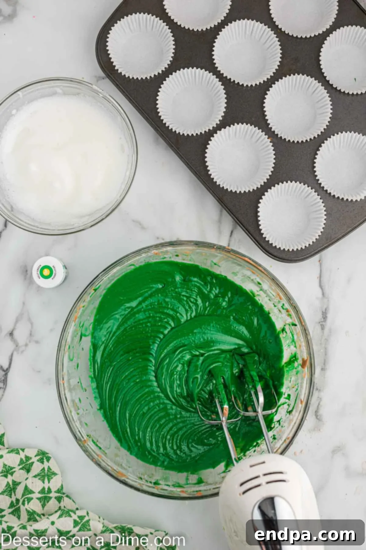 Green gel food coloring being mixed into the cupcake batter to achieve a vibrant hue.