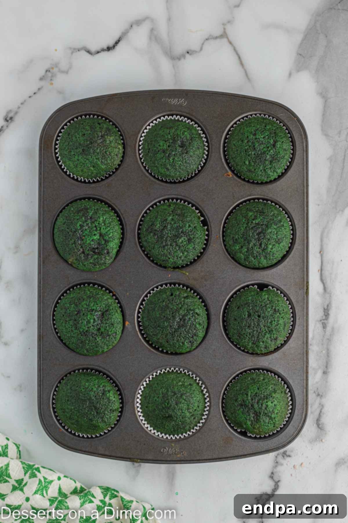 Freshly baked green velvet cupcakes cooling on a wire rack after being removed from the oven.
