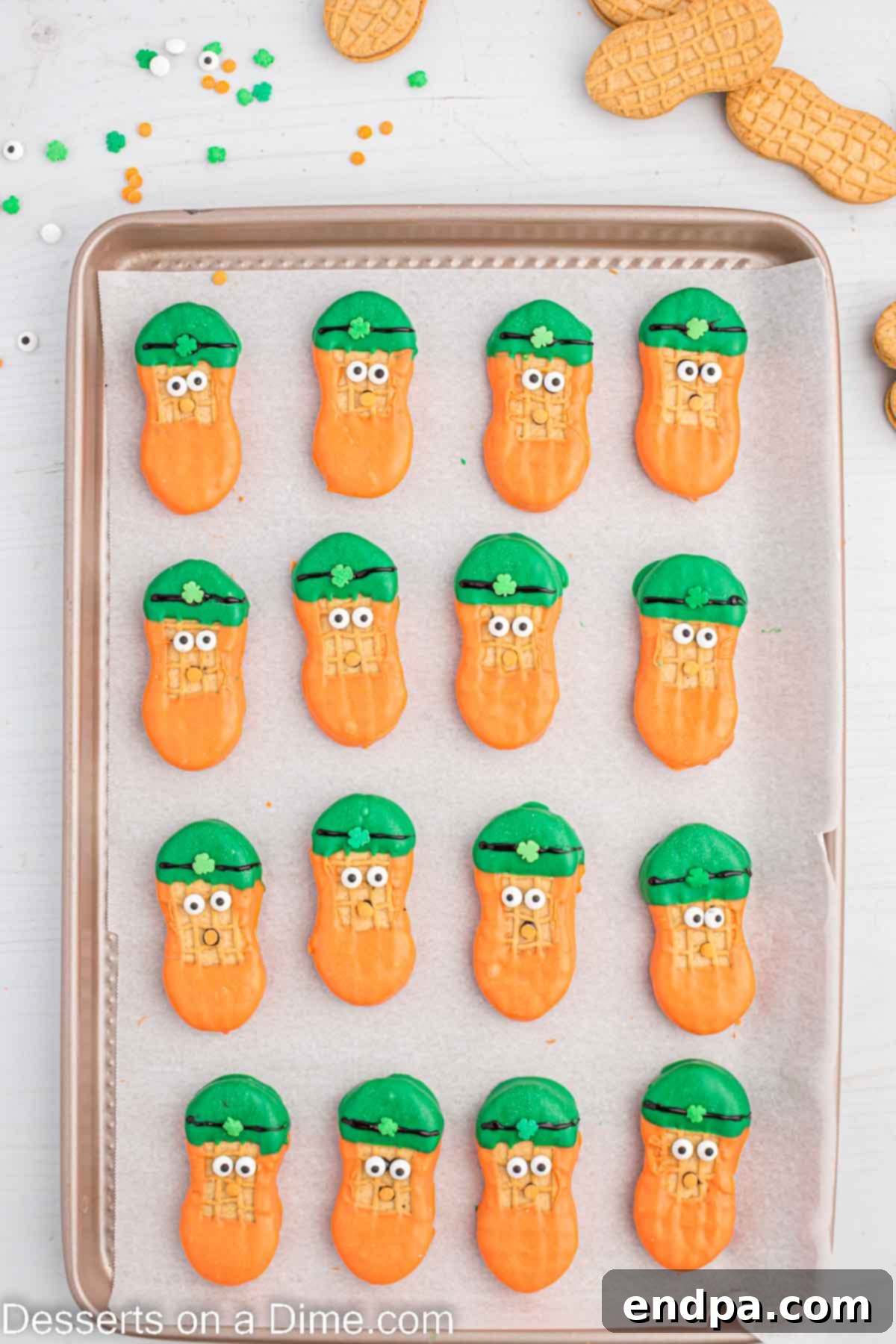 Lucky Leprechaun Bites 9 Candy eyes and an orange sprinkle nose being placed on a decorated leprechaun cookie.