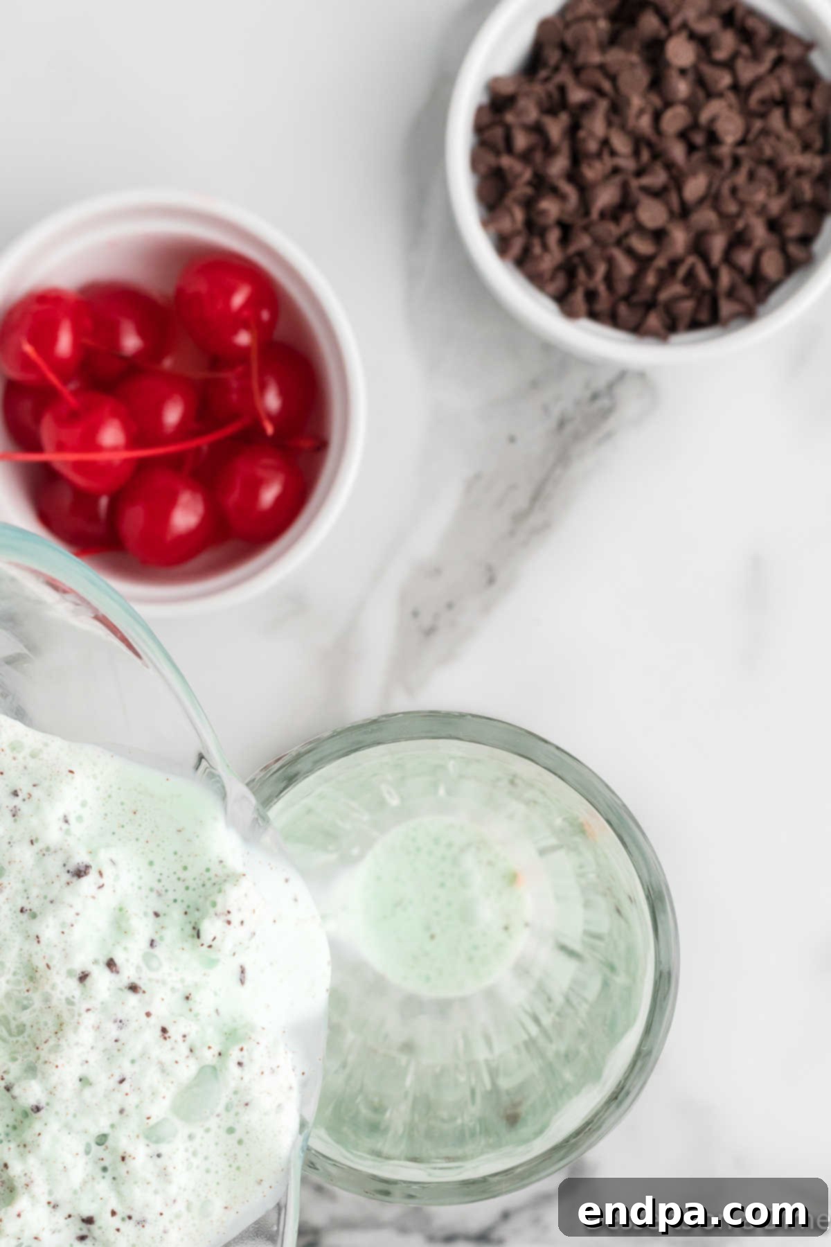 The freshly blended mint chocolate chip milkshake being poured from the blender into tall glasses.