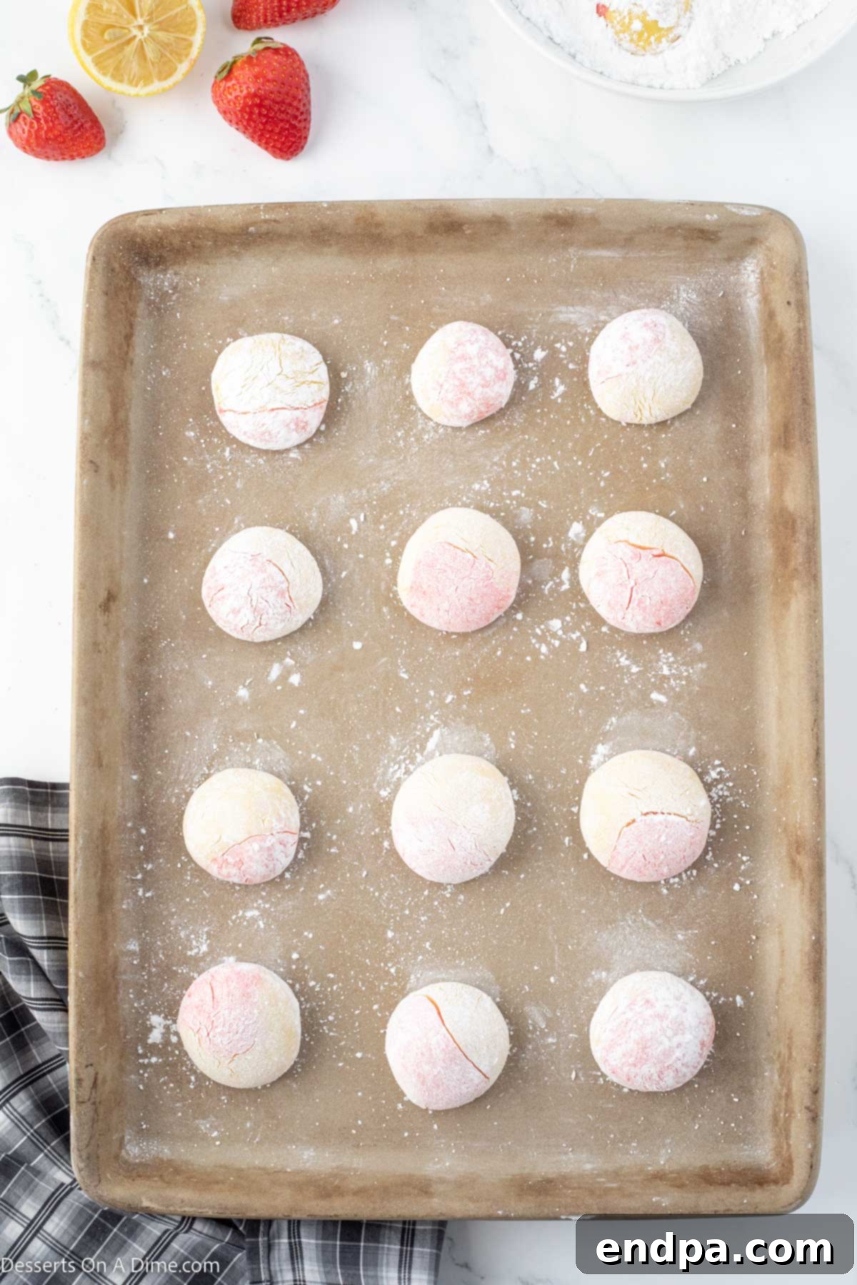 Tangy Strawberry Lemonade Cookies 7 Swirled cookie dough balls, coated in powdered sugar, evenly spaced on a baking sheet before baking.