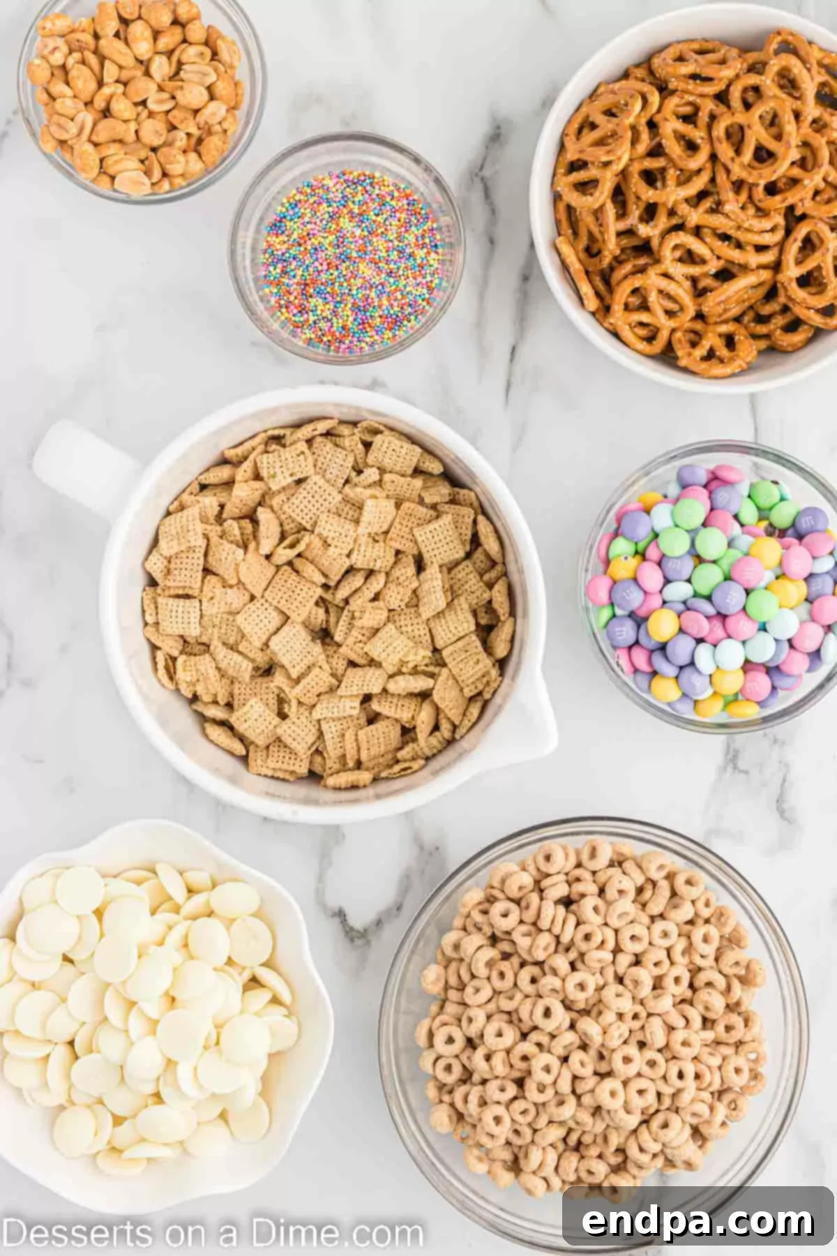 Bunny Magnet Mix 3 A flat lay of ingredients for Easter Bunny Bait, including pretzels, Honey Nut Cheerios, Chex cereal, salted peanuts, pastel M&M's, pastel sprinkles, and white chocolate wafers.