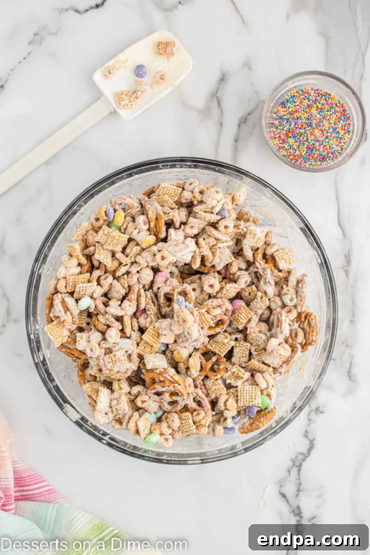 Bunny Magnet Mix 5 The mixed cereal, pretzels, peanuts, and M&M's in a bowl, coated in melted white chocolate, being stirred to ensure even coverage.