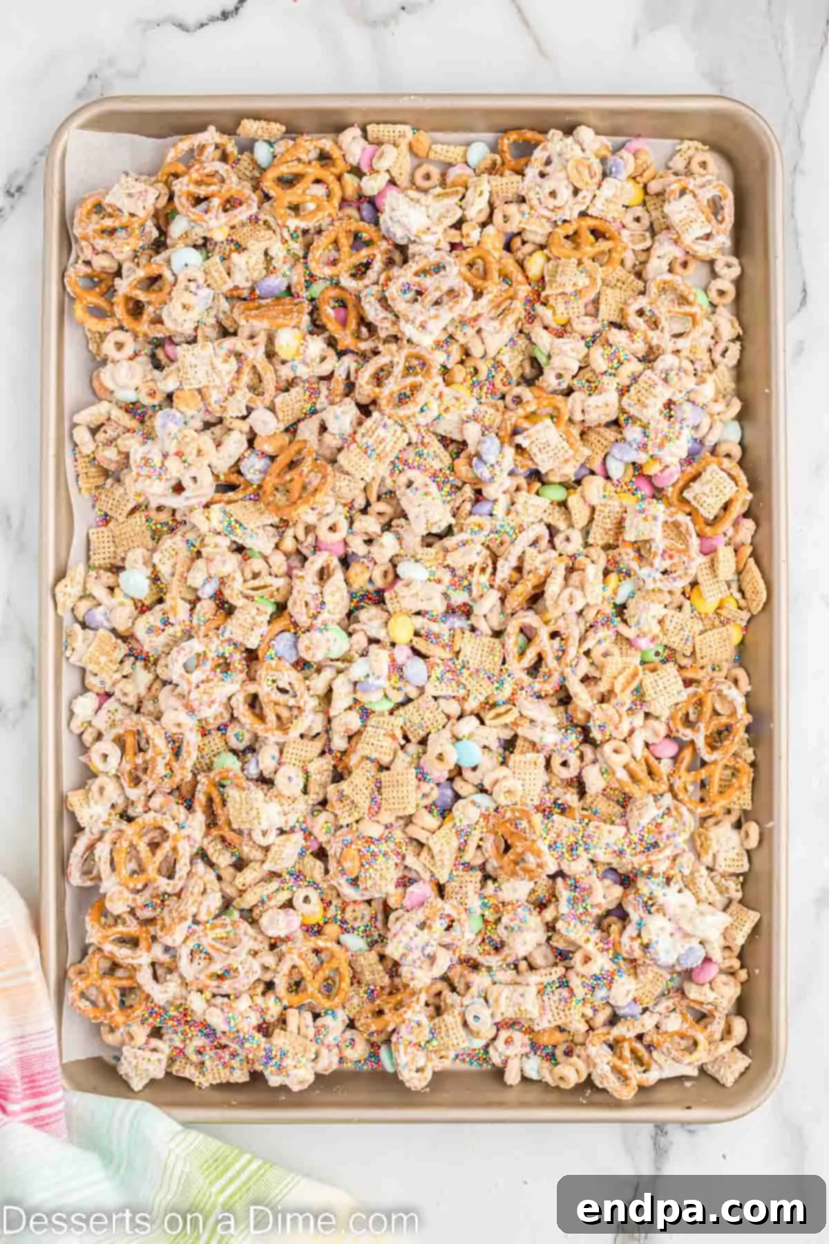 Bunny Magnet Mix 6 The chocolate-coated snack mix spread out on a sheet pan lined with wax paper, topped with a generous amount of pastel sprinkles.