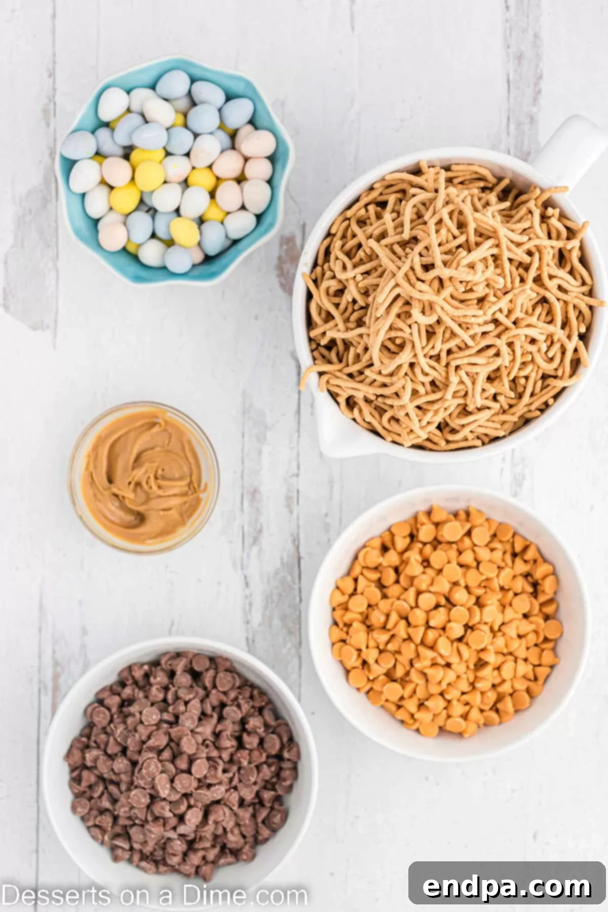 Ingredients for Birds nest cookies- chocolate chips, butterscotch chips, creamy peanut butter, chow mein noodles, and Cadbury mini eggs, laid out on a table.