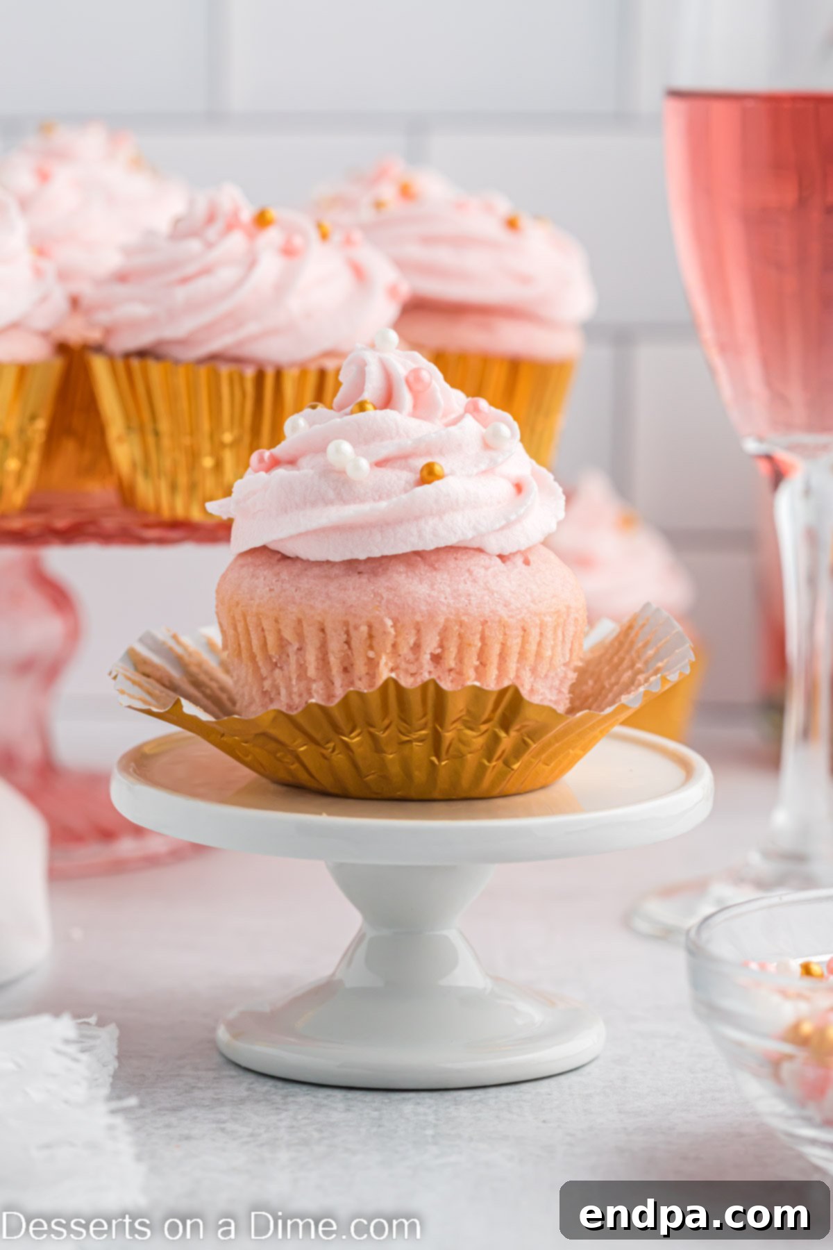 Two beautifully frosted Pink Champagne Cupcakes, adorned with festive sprinkles, elegantly presented on a white plate, ready to be enjoyed.