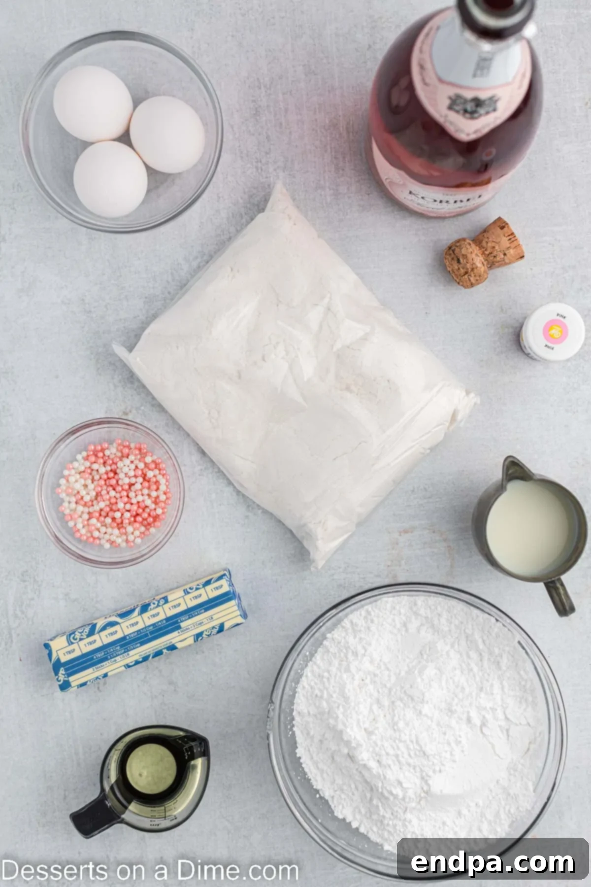 A beautiful flat lay of all the essential ingredients for making Pink Champagne Cupcakes: white cake mix, sparkling pink champagne, vegetable oil, fresh egg whites, vibrant pink food coloring, softened butter, powdered sugar, and a splash of milk.