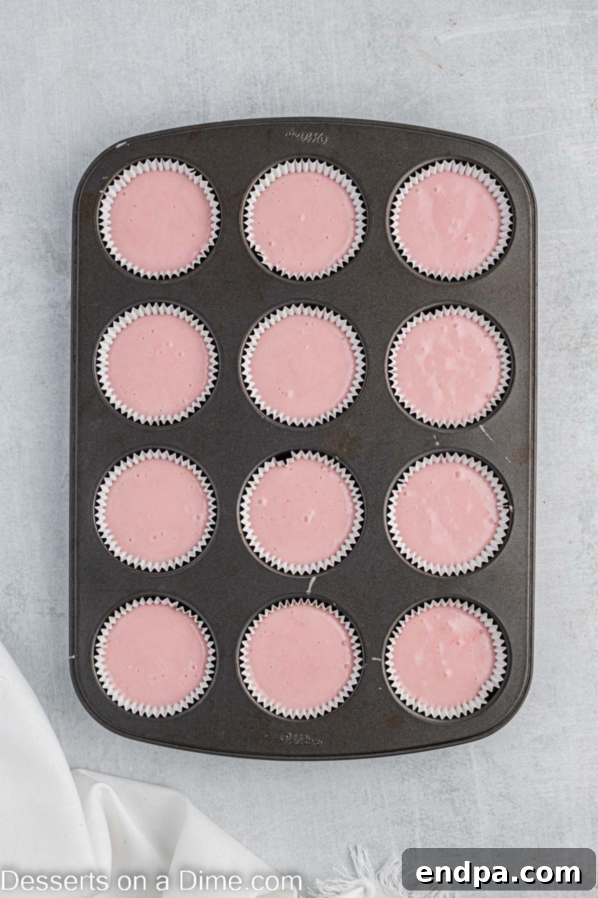 Muffin tins filled evenly with the vibrant pink cupcake batter, ready for baking.