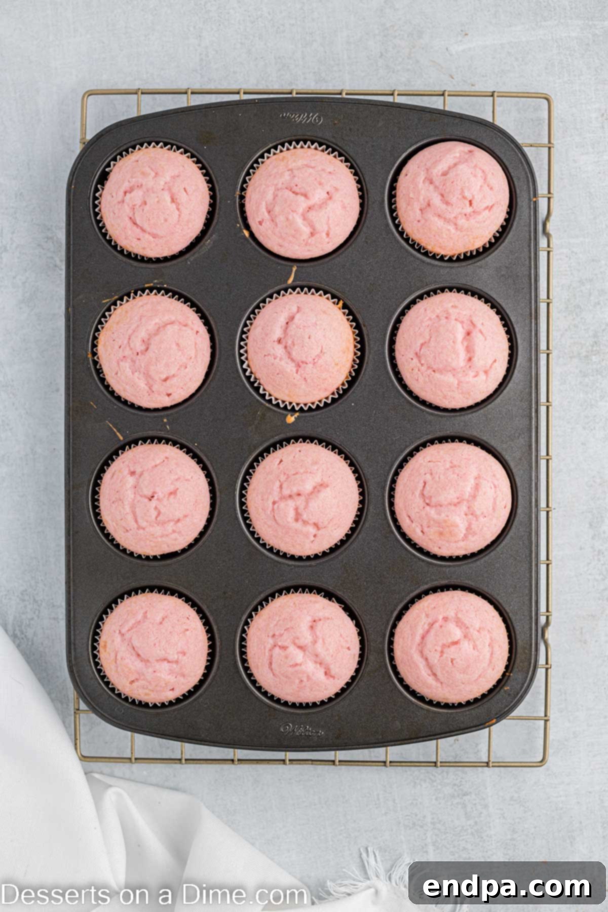 Freshly baked pink cupcakes in their liners, still in the muffin pan, with a golden-brown top.