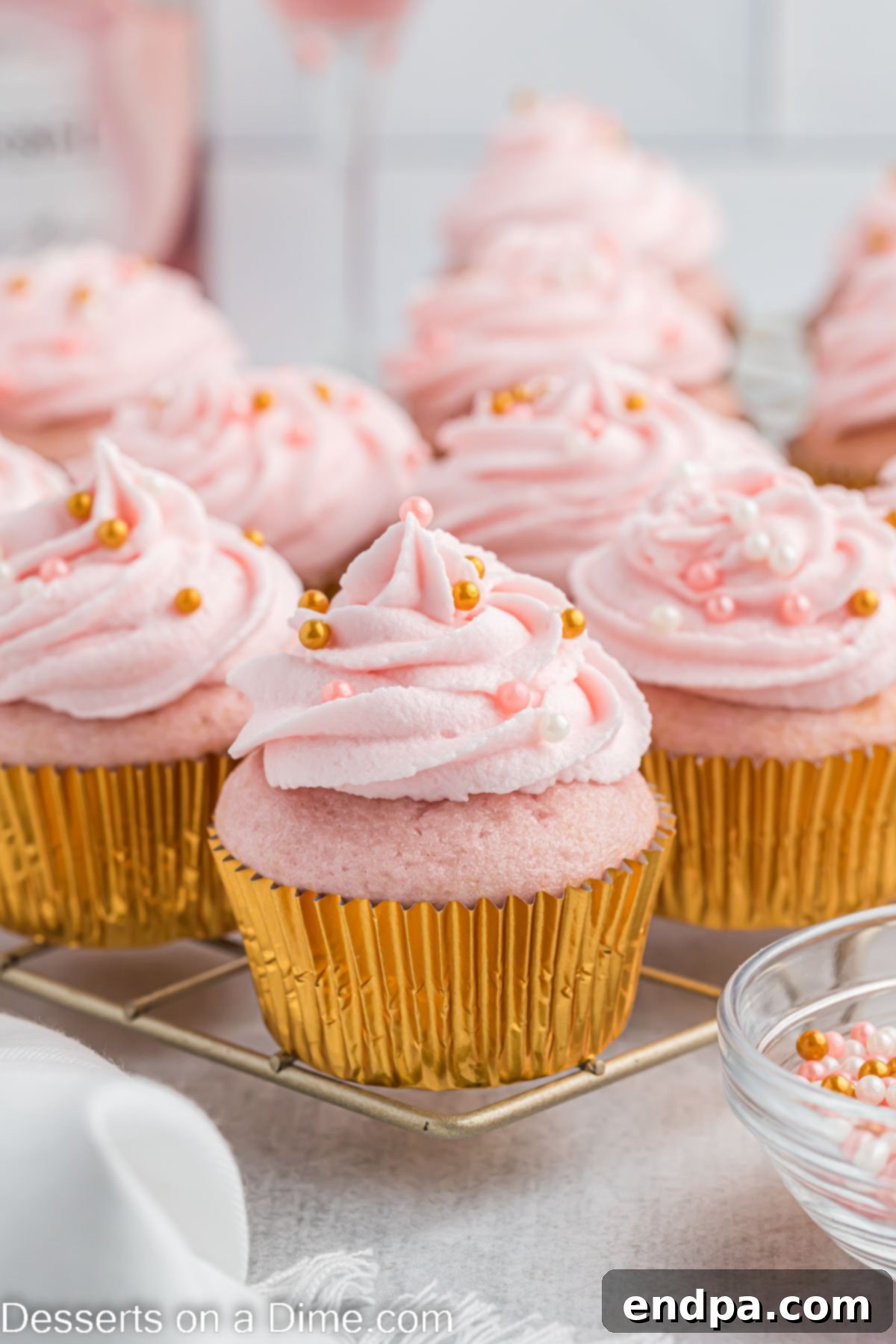 Beautifully frosted Pink Champagne Cupcakes adorned with sprinkles, arranged on a wire rack.
