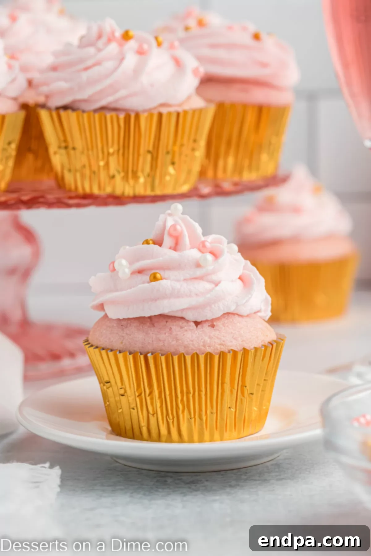A single Pink Champagne Cupcake, beautifully frosted and sprinkled, displayed on an elegant white plate.