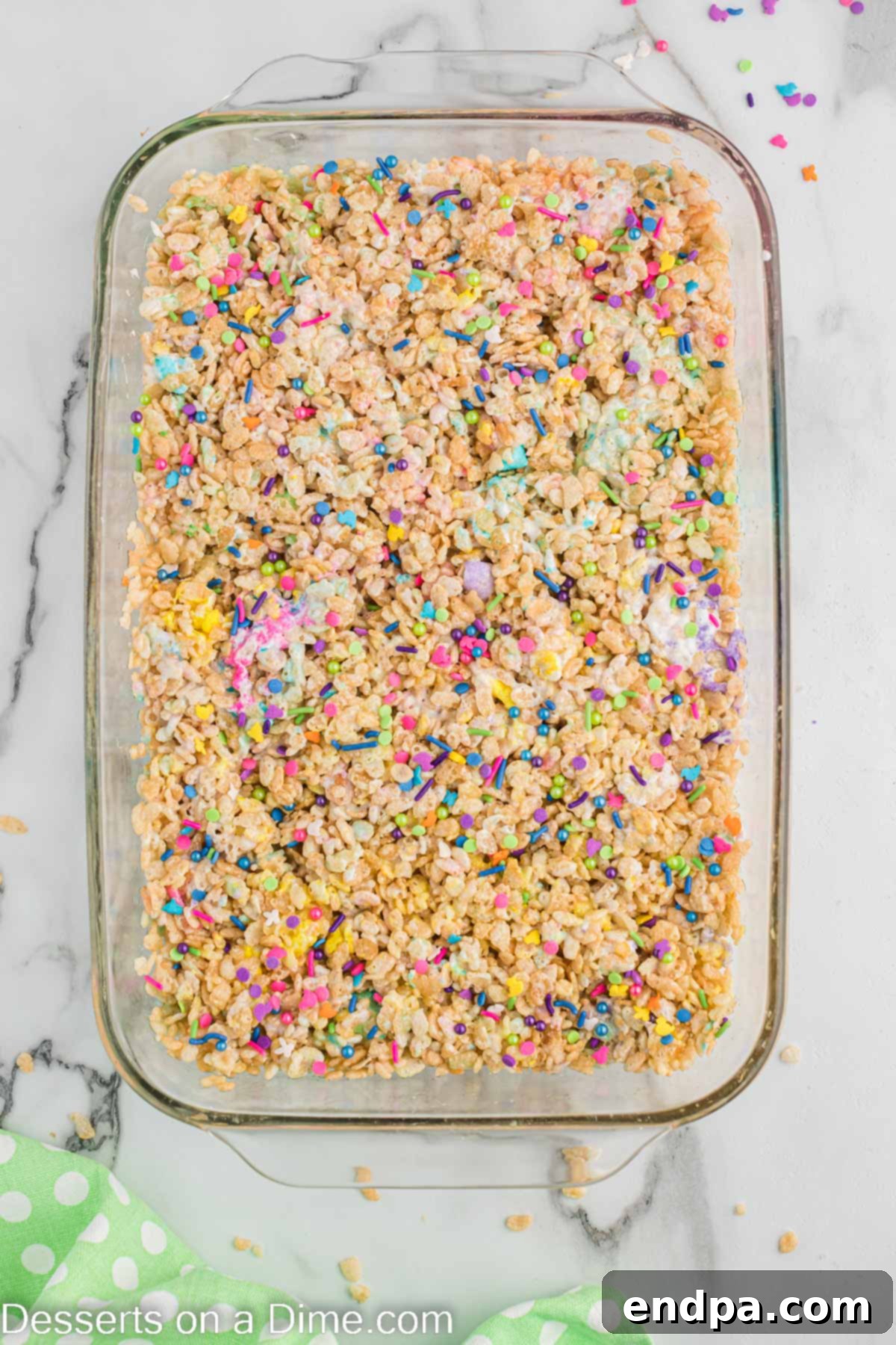 Pastel sprinkles generously scattered over the pressed cereal mixture in the baking dish, ready for setting.