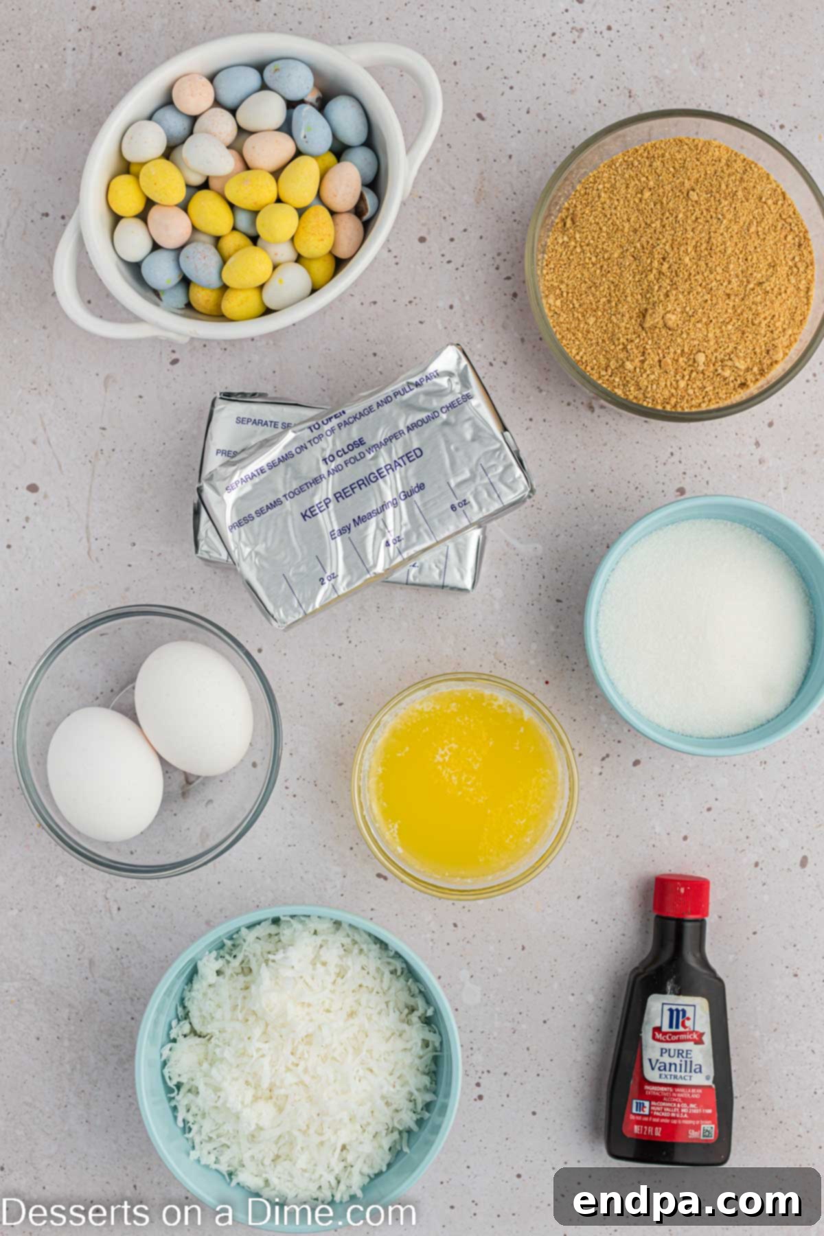 Hoppy Easter Cheesecake Bites 3 A flat lay of all ingredients needed for Mini Easter Cheesecakes: graham cracker crumbs, melted butter, softened cream cheese, granulated sugar, vanilla extract, large eggs, shredded coconut, and Robin Eggs candy.