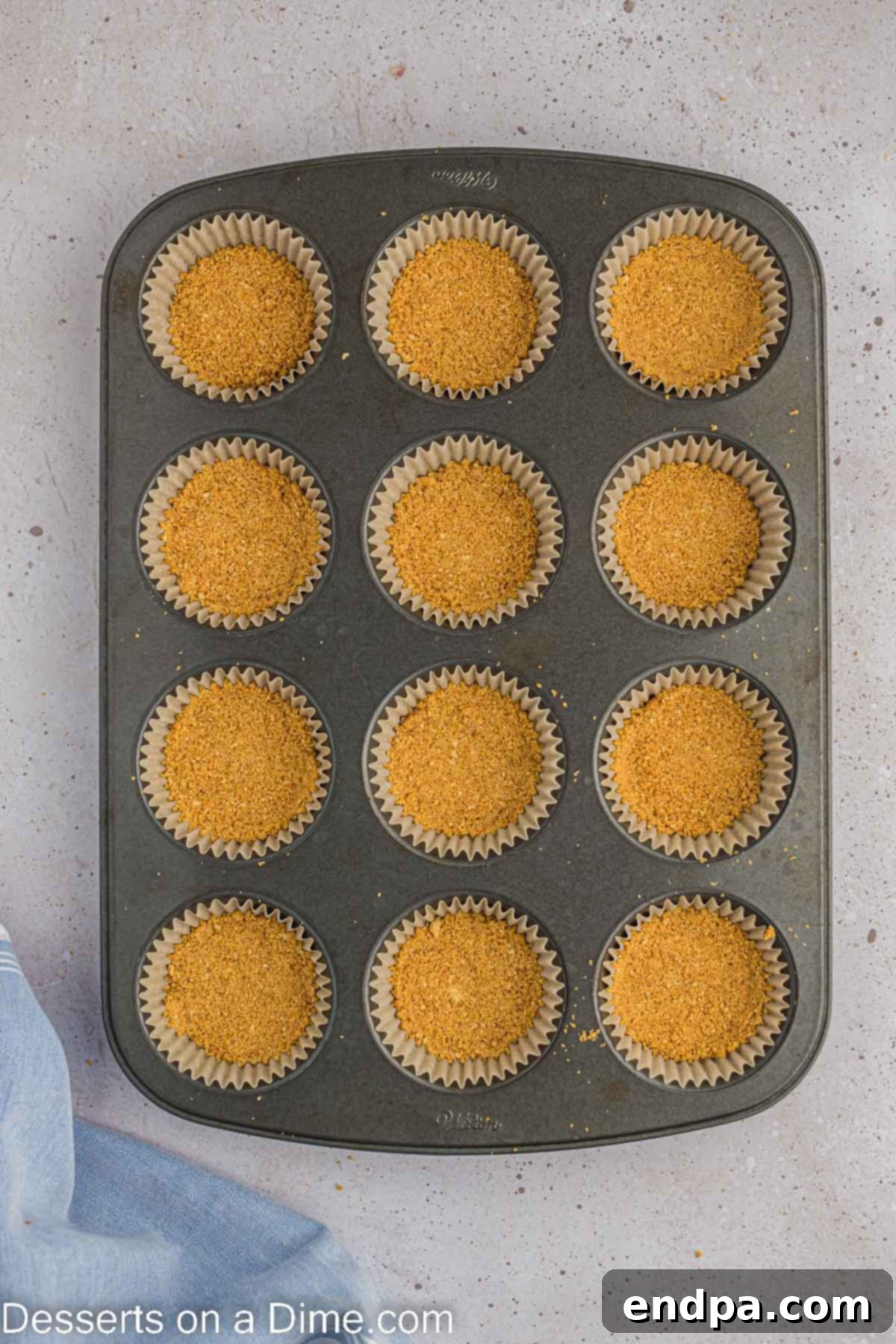 Hoppy Easter Cheesecake Bites 5 Graham cracker crumbs pressed into paper liners inside a muffin tin, forming the cheesecake crust.