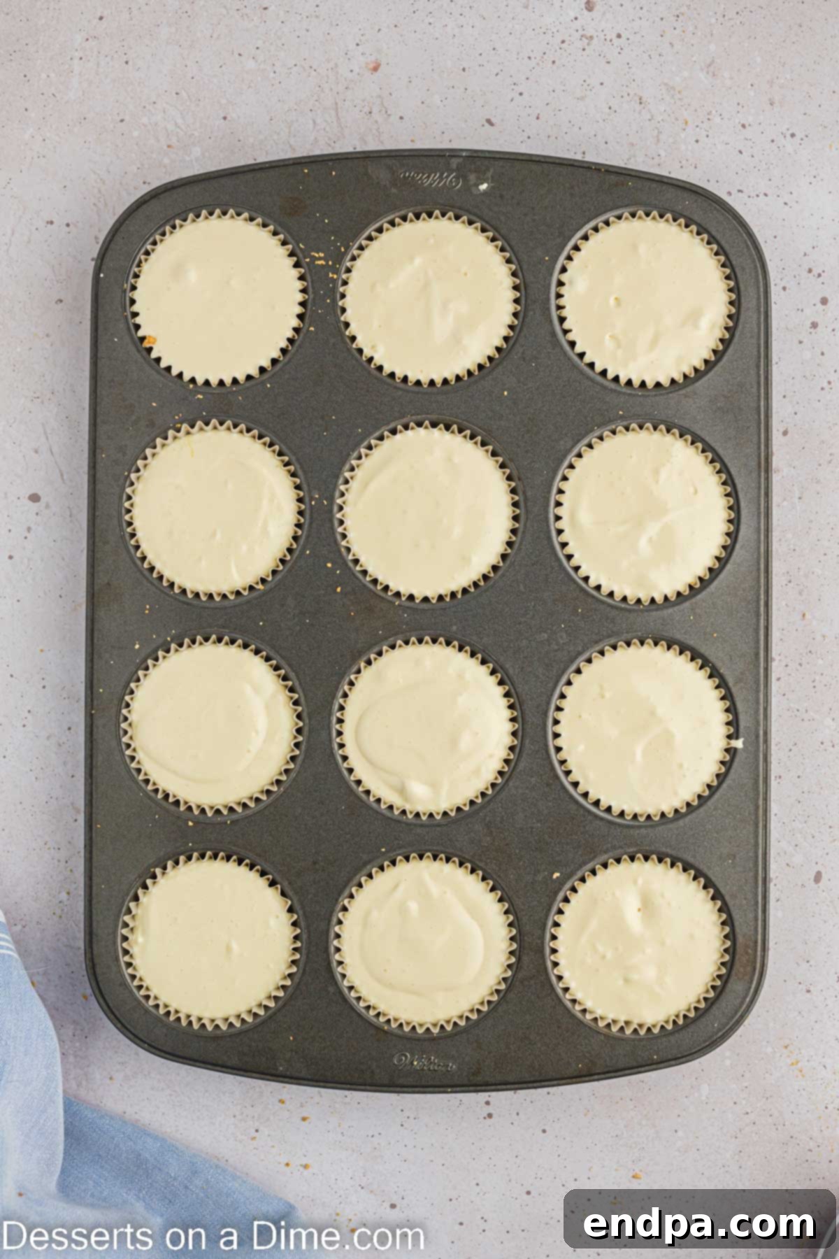Hoppy Easter Cheesecake Bites 7 Cheesecake batter being spooned evenly over the graham cracker crusts in a muffin tin.