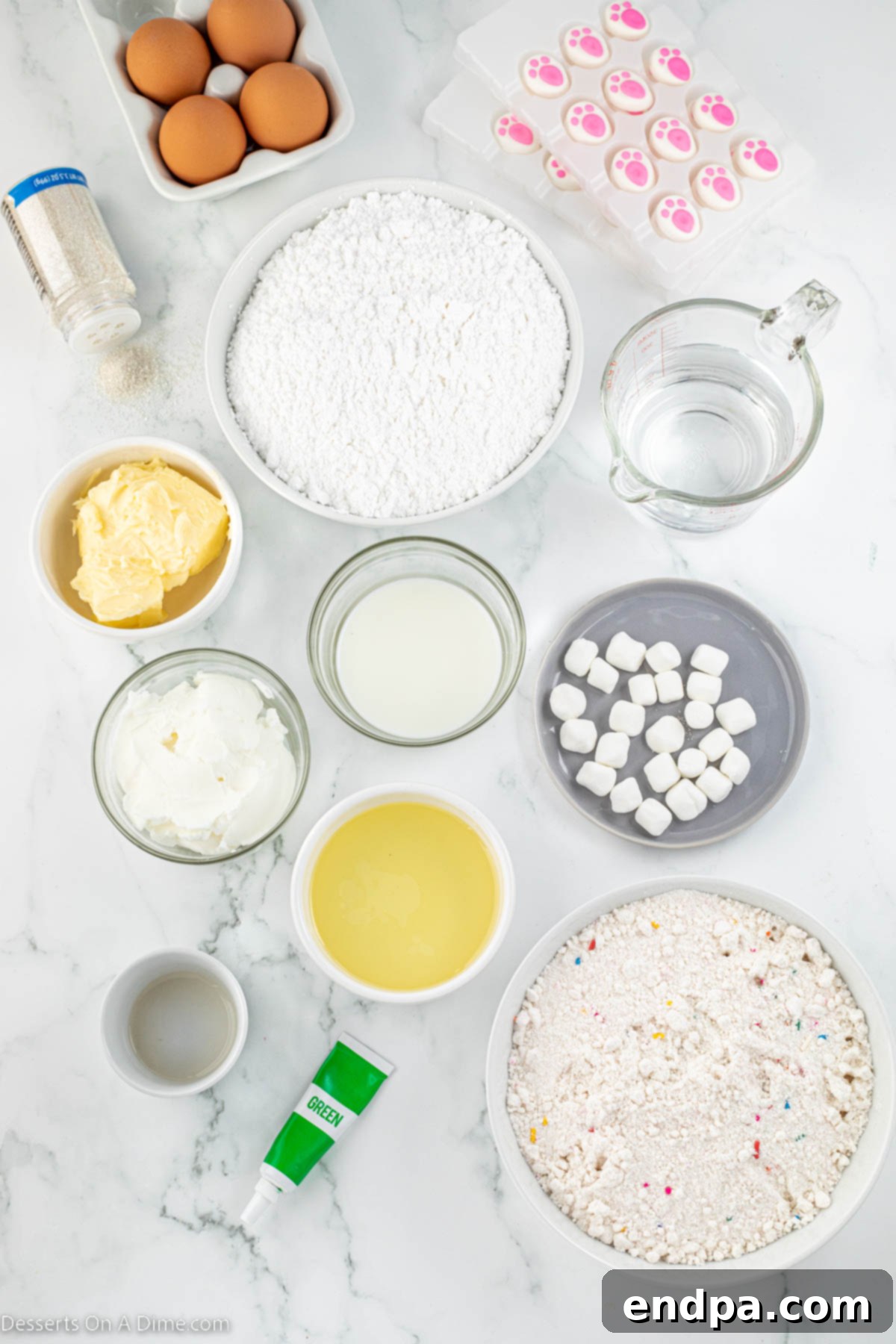 Ingredients spread out for Bunny Butt Cupcakes including shortening, butter, vanilla extract, powdered sugar, milk, green gel food coloring, white sanding sugar, mini marshmallows, and pre-made bunny feet decorations.