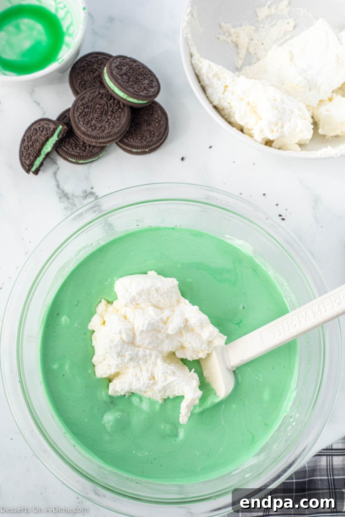 Emerald Mint Delight 8 Whipped cream being gently folded into the green marshmallow-liqueur mixture in a mixing bowl, creating a light and airy pie filling.