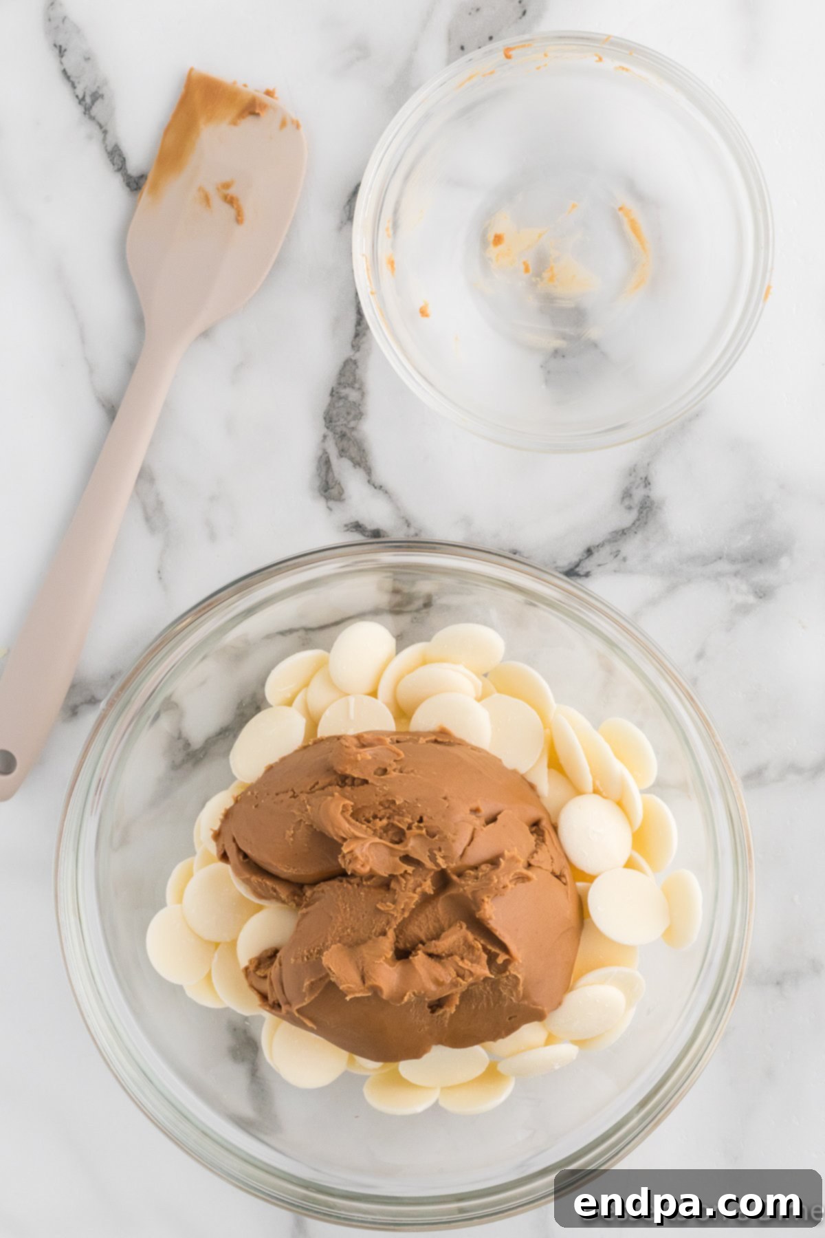 Cookie Butter being added to melted white chocolate in a bowl.