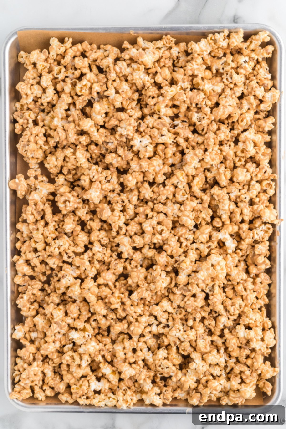 Popcorn coated in a cookie butter and white chocolate mixture, spread evenly on a baking sheet to harden.
